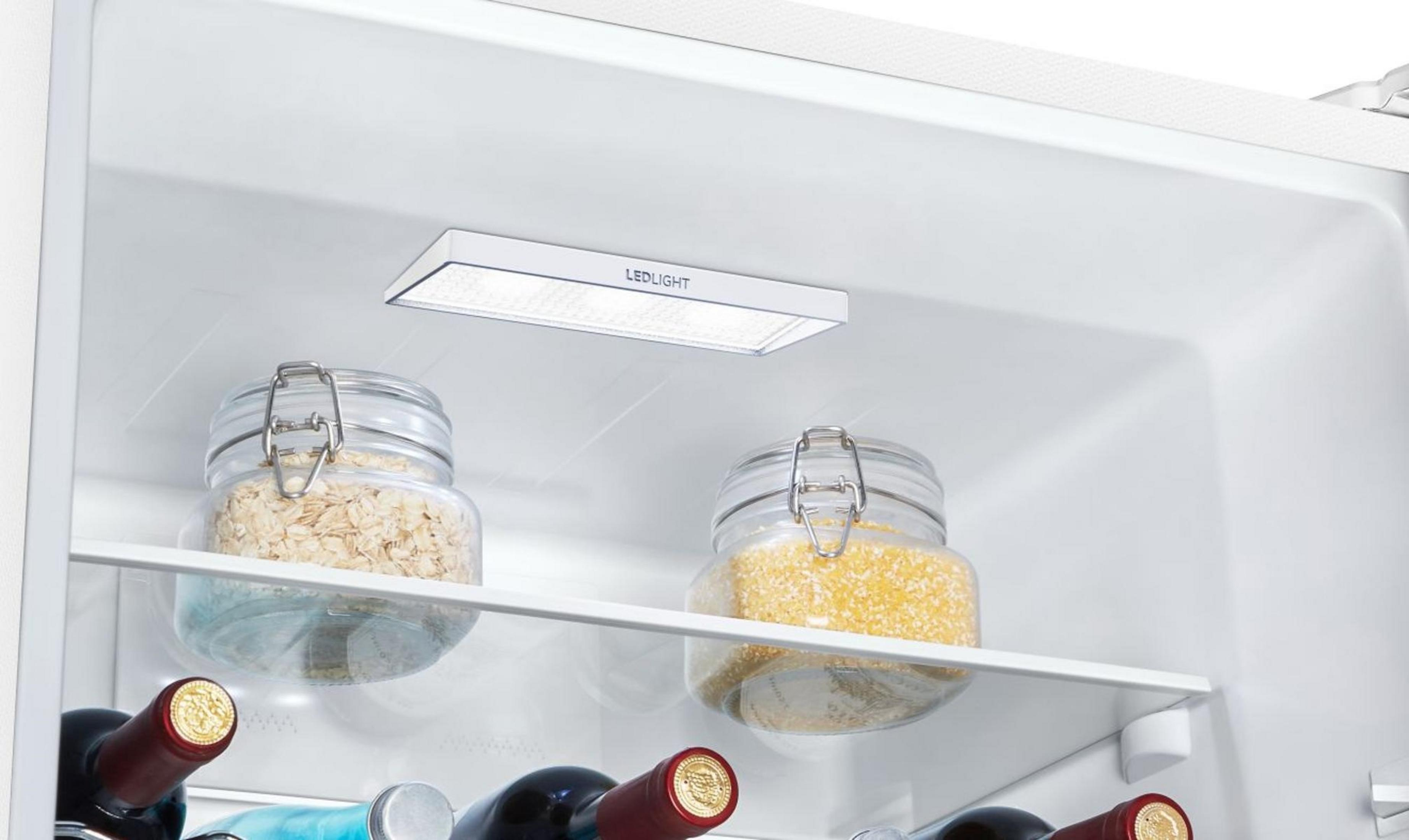 In einem Kühlschrank befinden sich zwei Gläser mit Inhalt auf einem Regal. Weinflaschen sind unten. Oben ist eine LED-Leuchte montiert.