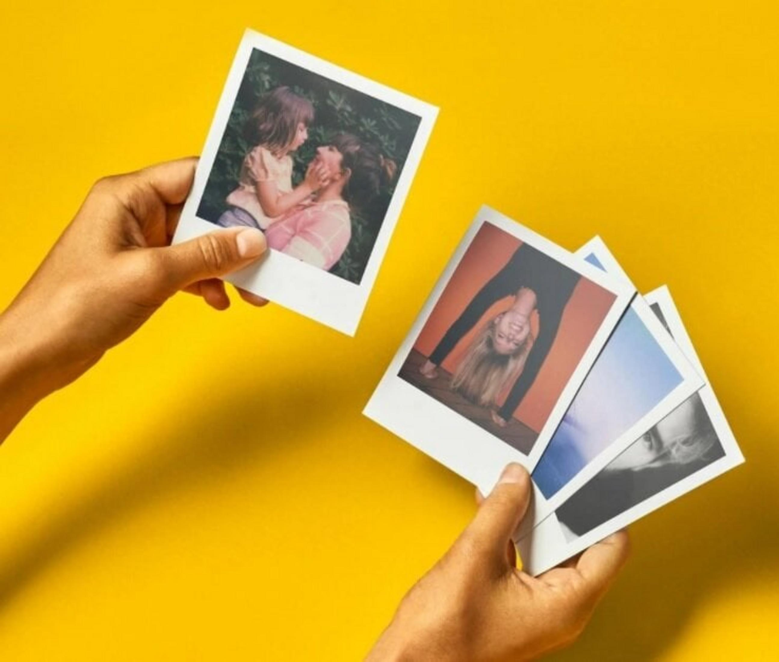 Ręce trzymające zdjęcia polaroid na żółtym tle. Zdjęcia przedstawiają matkę z dzieckiem oraz kobietę uprawiającą jogę.
