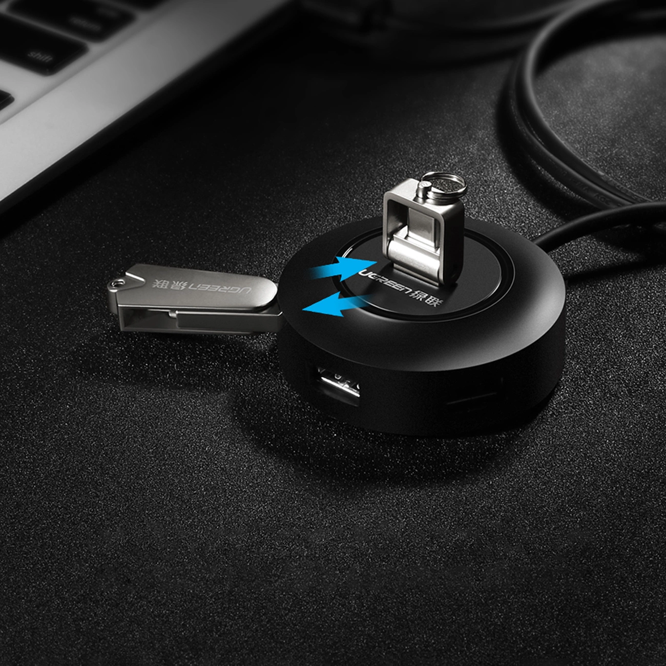 Czarny hub USB ze srebrnym metalowym portem i srebrnym złączem USB. Klawiatura laptopa znajduje się w tle.