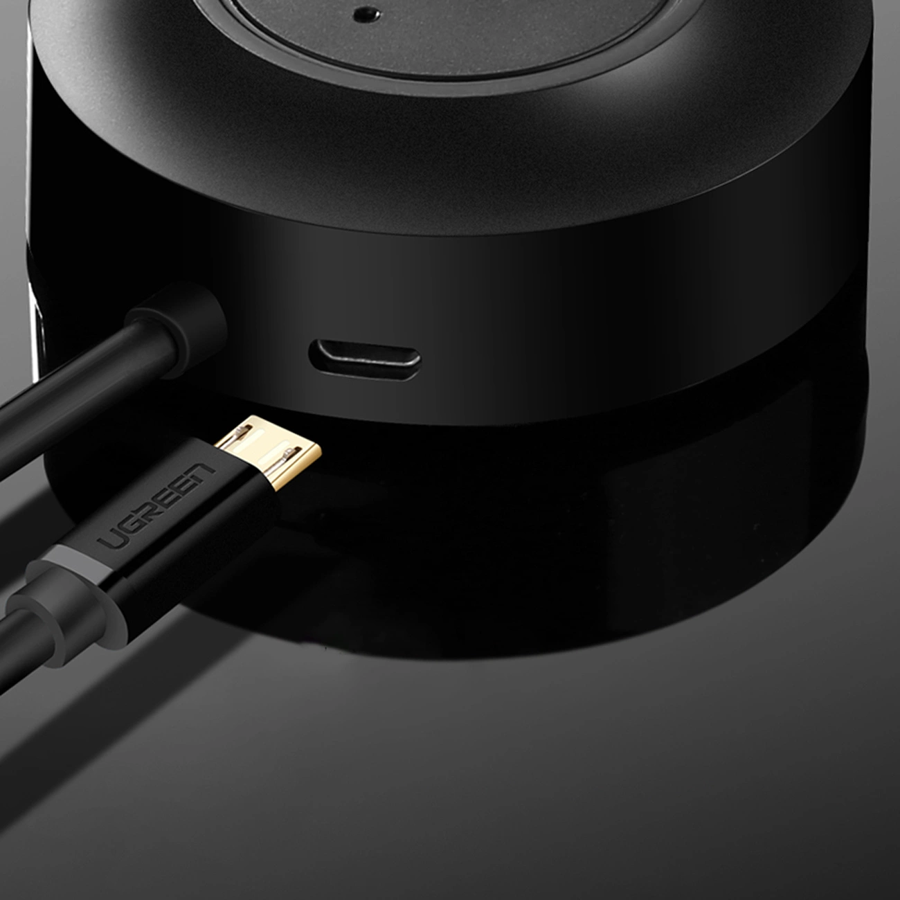 Zbliżenie czarnego urządzenia z podłączonym kablem USB. Kabel jest oznaczony jako UGREEN i ma złoty konektor.