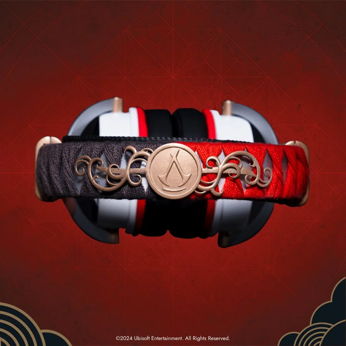 Słuchawki z czerwono-czarnym designem. Design obejmuje złote logo Assassin's Creed i elementy dekoracyjne na czerwonym tle.