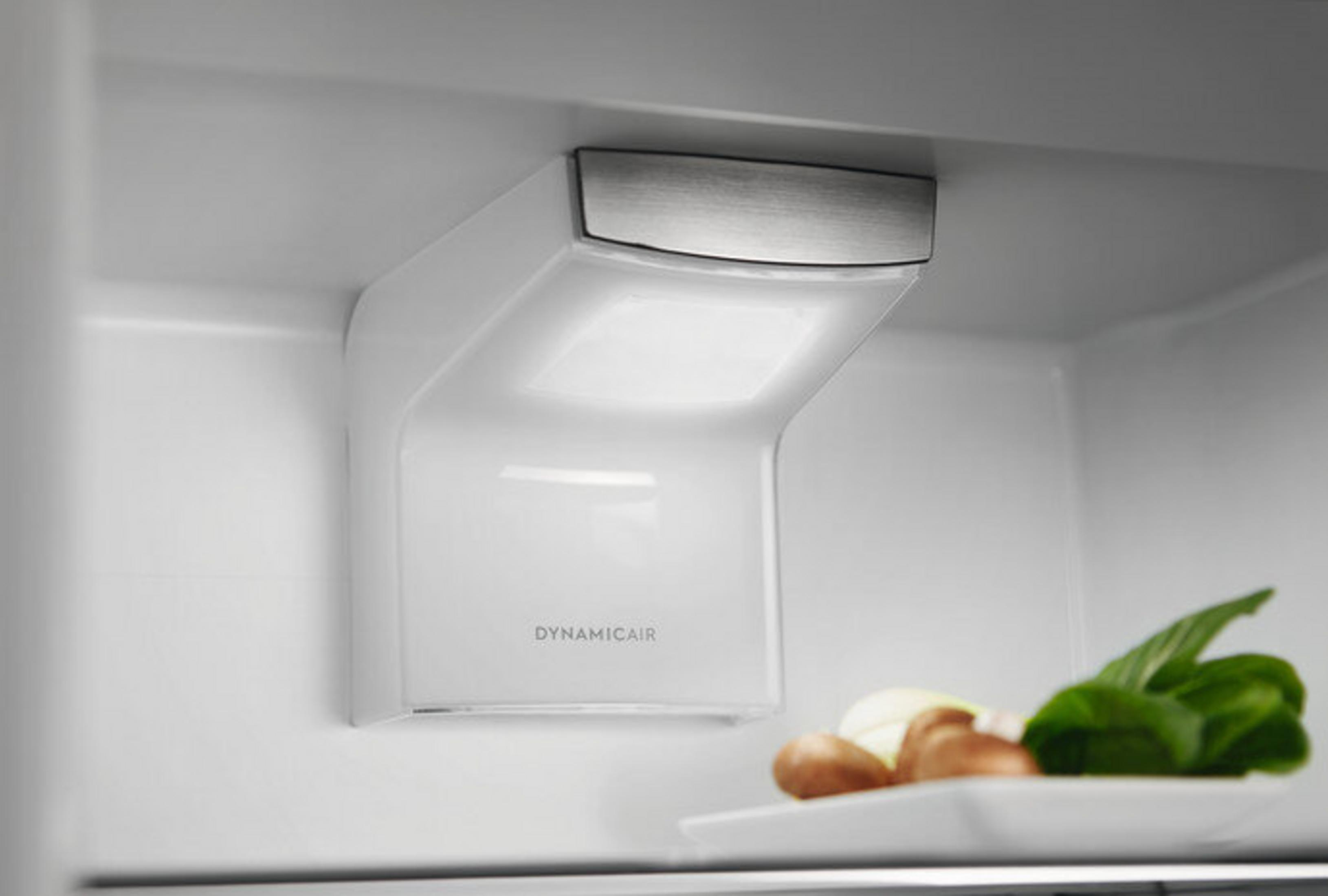 All'interno di un frigorifero, una presa d'aria bianca con luce, verdure su un piatto sotto.