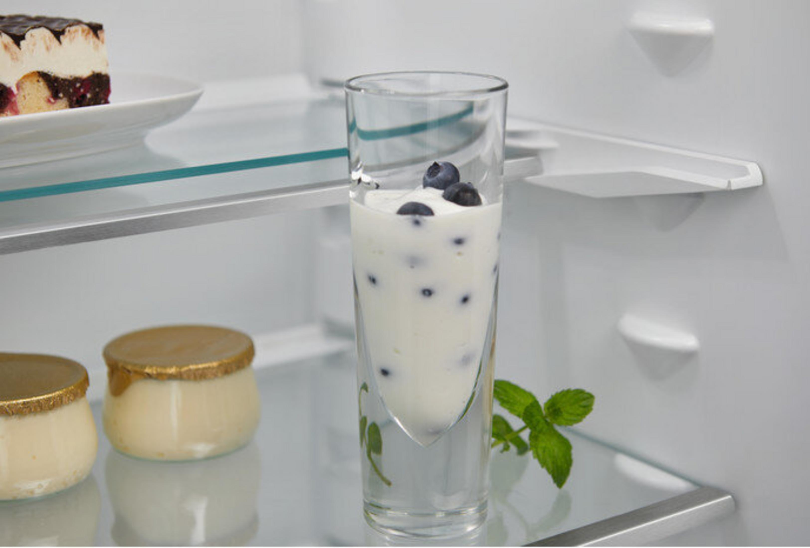 Un bicchiere con yogurt e mirtilli. Ci sono due vasetti e una torta su un piatto. Foglie di menta a destra.