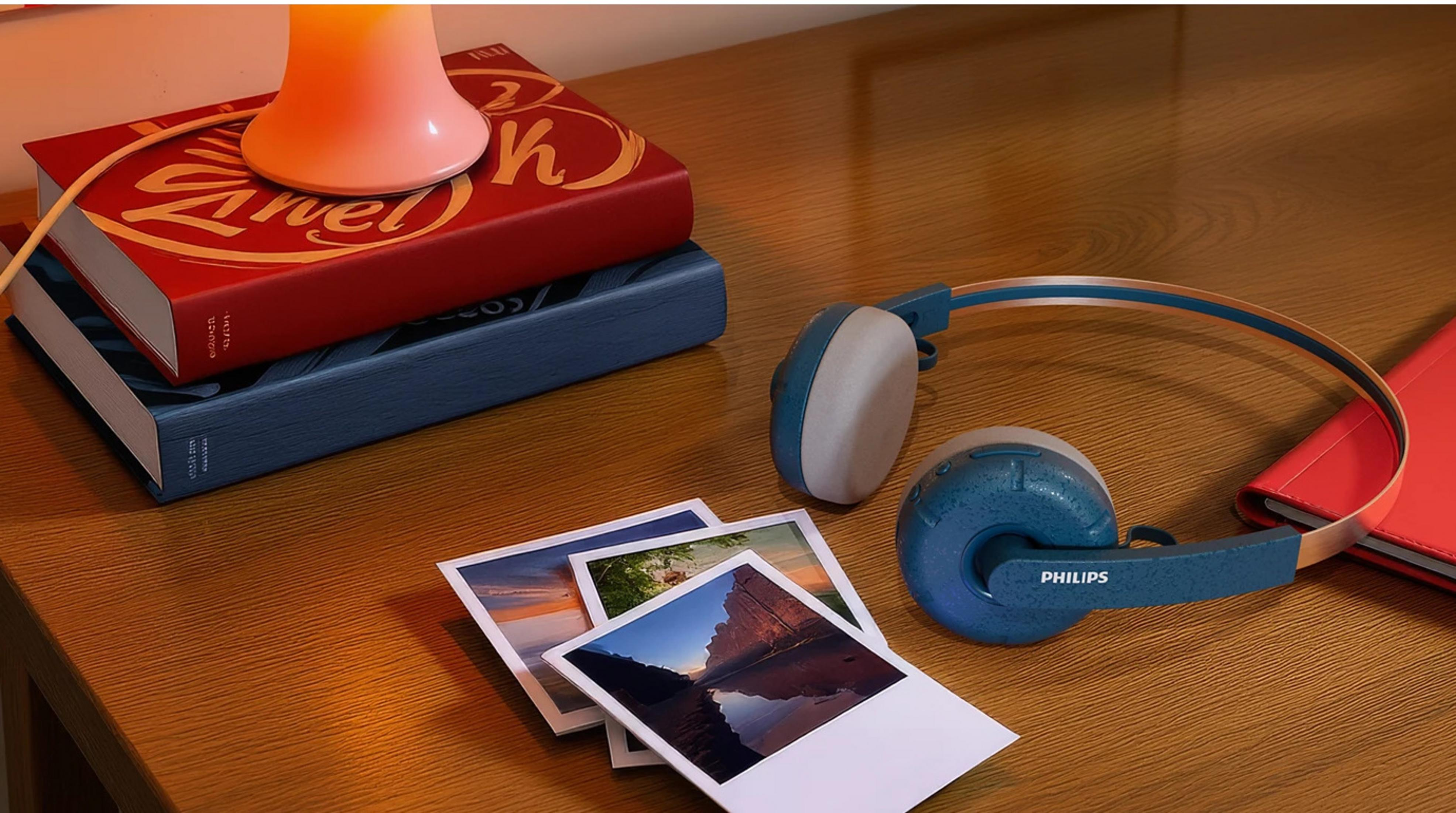 Un bureau avec des livres, un casque, des photos et une lampe. Le casque est bleu et blanc. Les livres sont rouges et bleus.