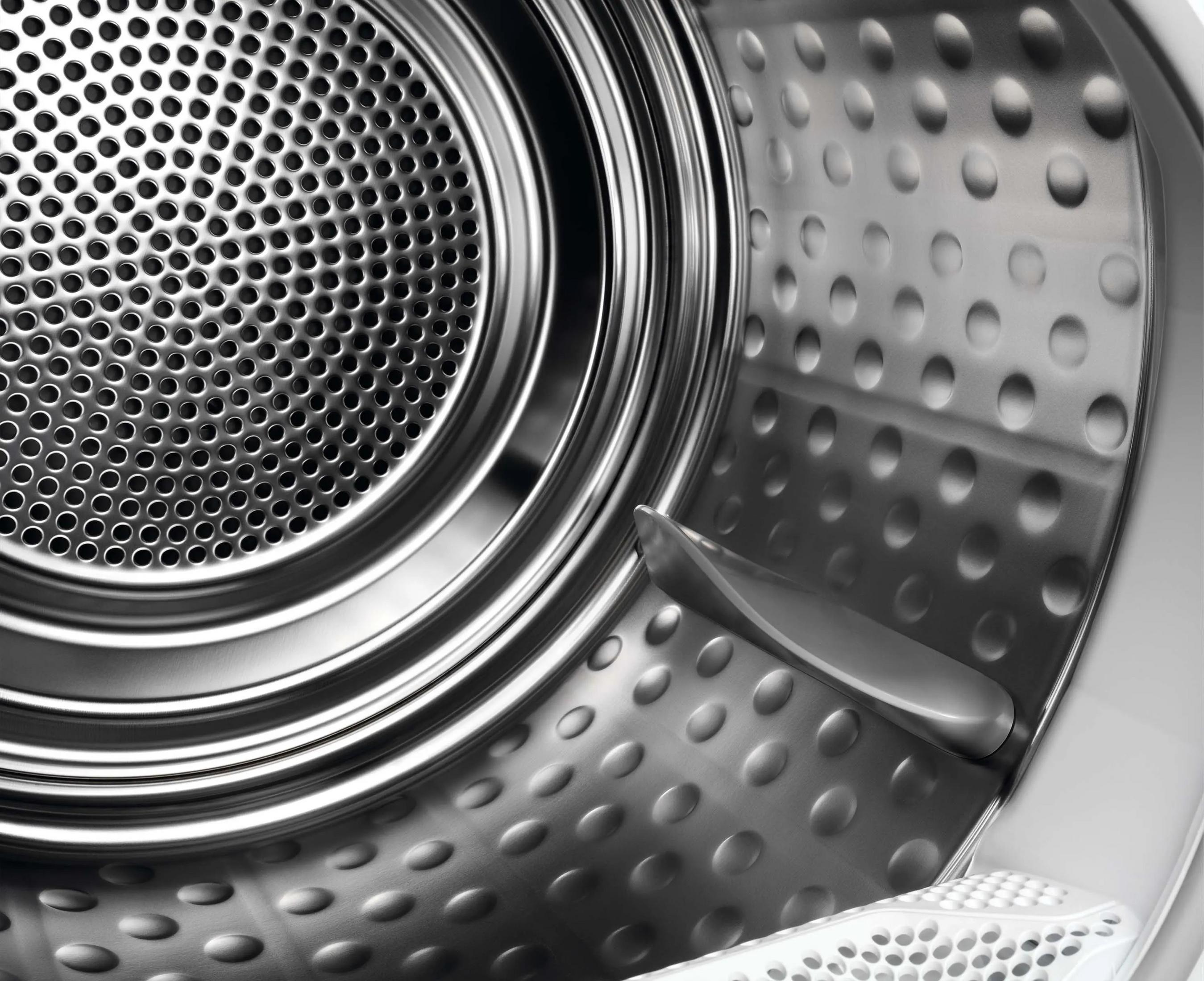 Zbliżenie wnętrza bębna suszarki. Po lewej stronie perforowana metalowa siatka, srebrne wnętrze z wypukłościami.