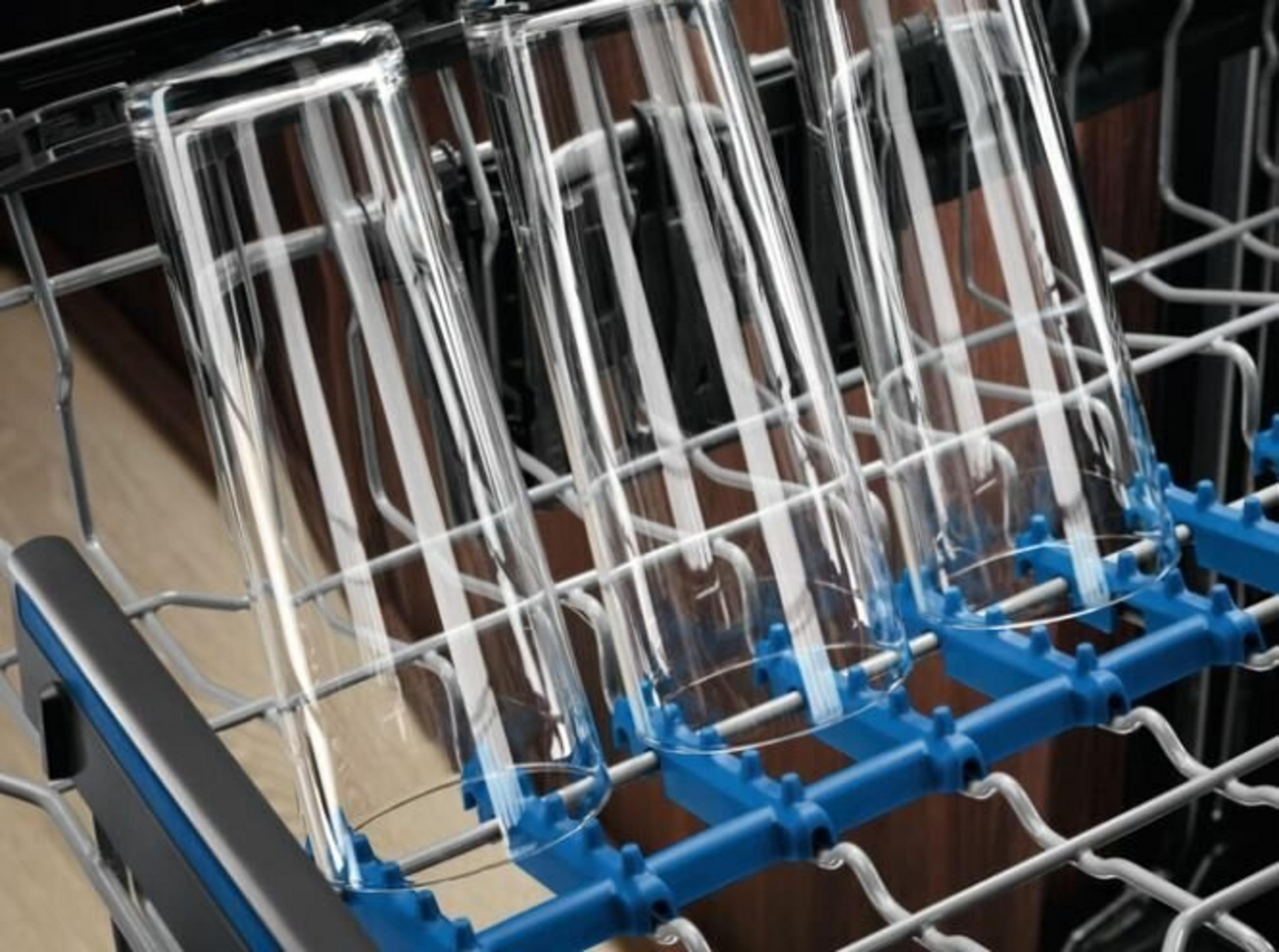 Vasos transparentes en una rejilla de lavavajillas azul y gris. El fondo es de madera.