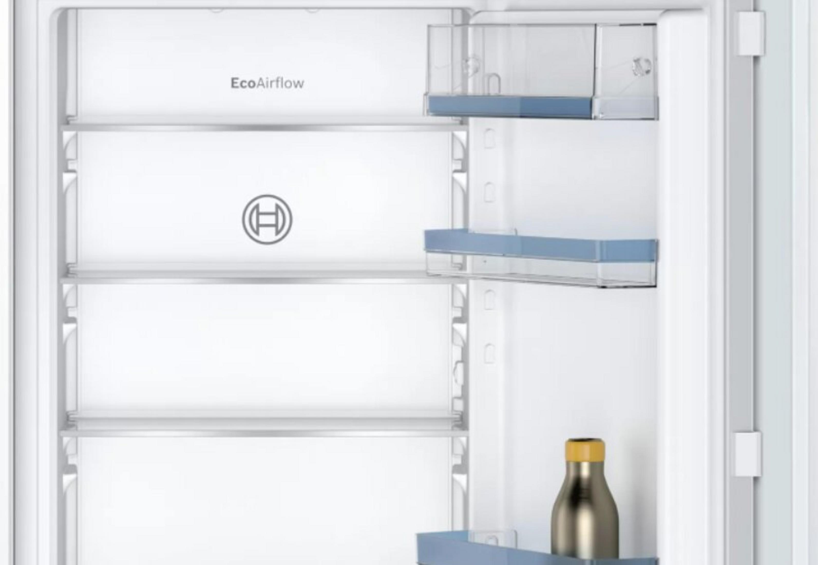 Otwarty środek lodówki. Widoczne półki, butelka i logo Bosch. Białe drzwi.
