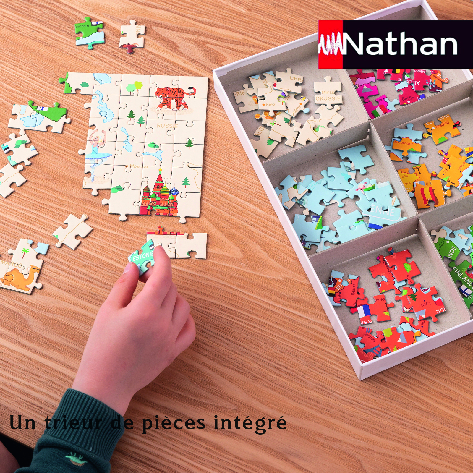 Die Hand eines Kindes legt ein Puzzleteil in ein teilweise zusammengesetztes Weltkartenpuzzle. Weitere Teile und eine Box sind vorhanden.