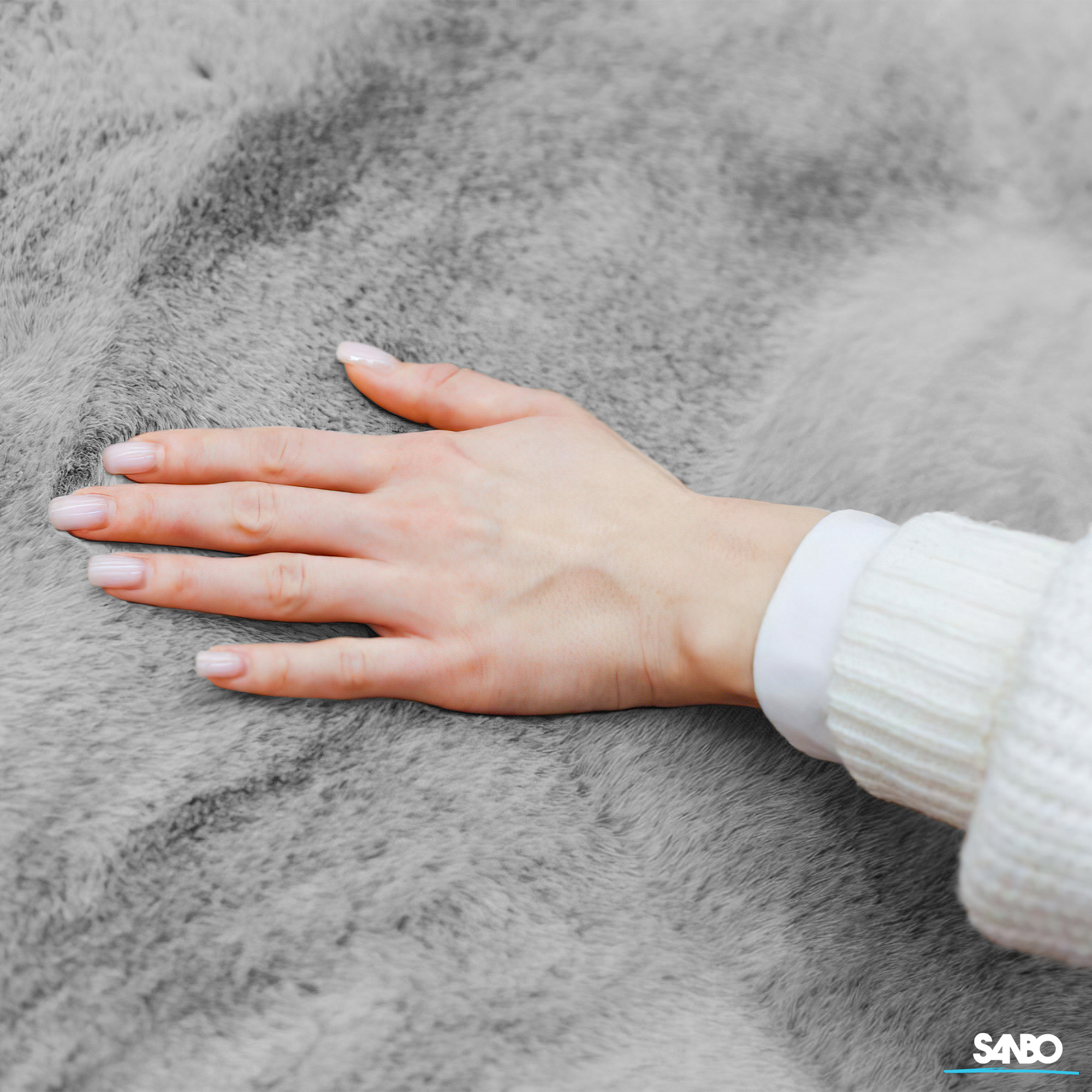 A hand rests on gray fur. The person wears a white sweater and a white shirt. The nails are painted.