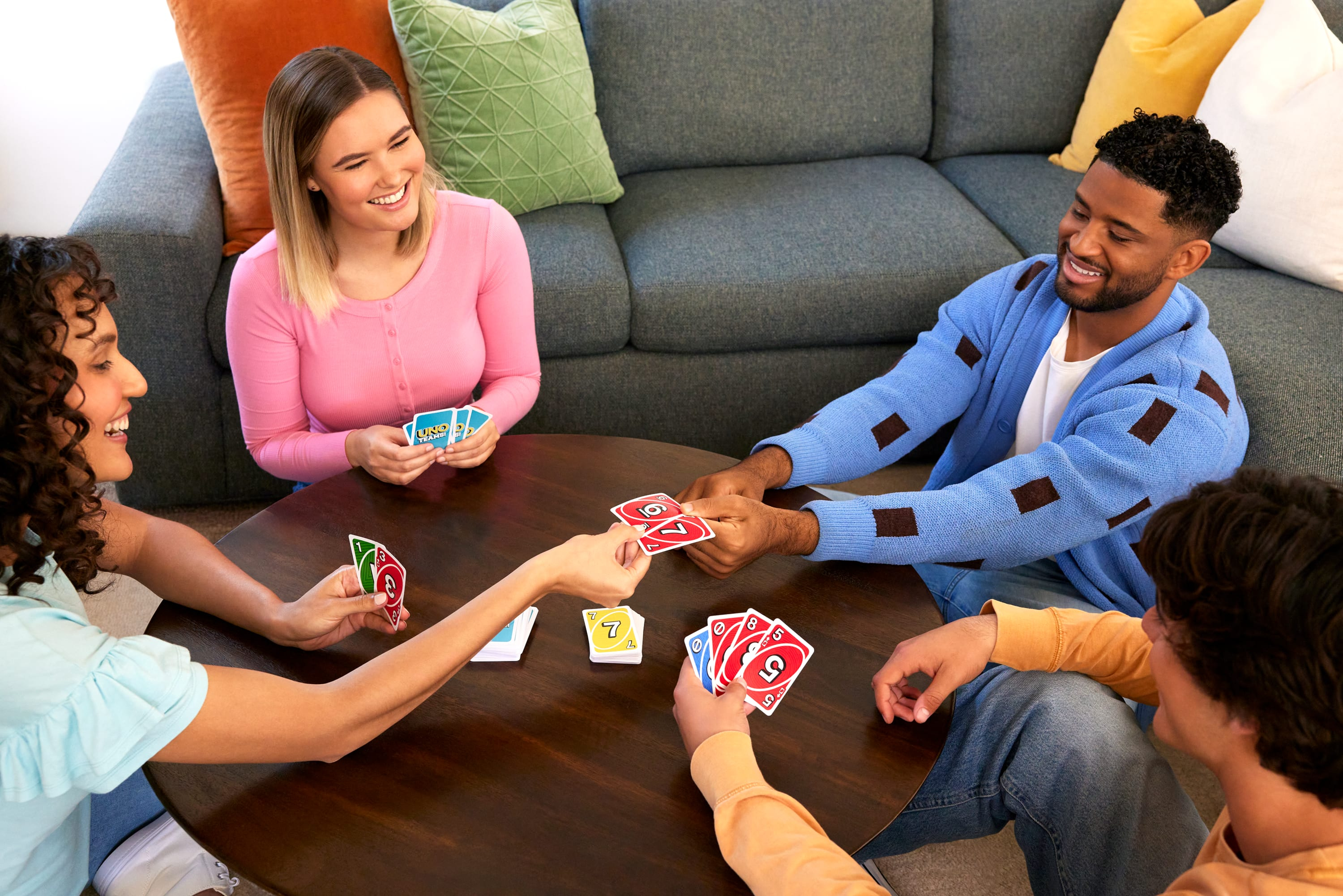 Cuatro personas jugando a las cartas. Una mujer sonríe, sosteniendo cartas. Otros sostienen cartas, jugando.