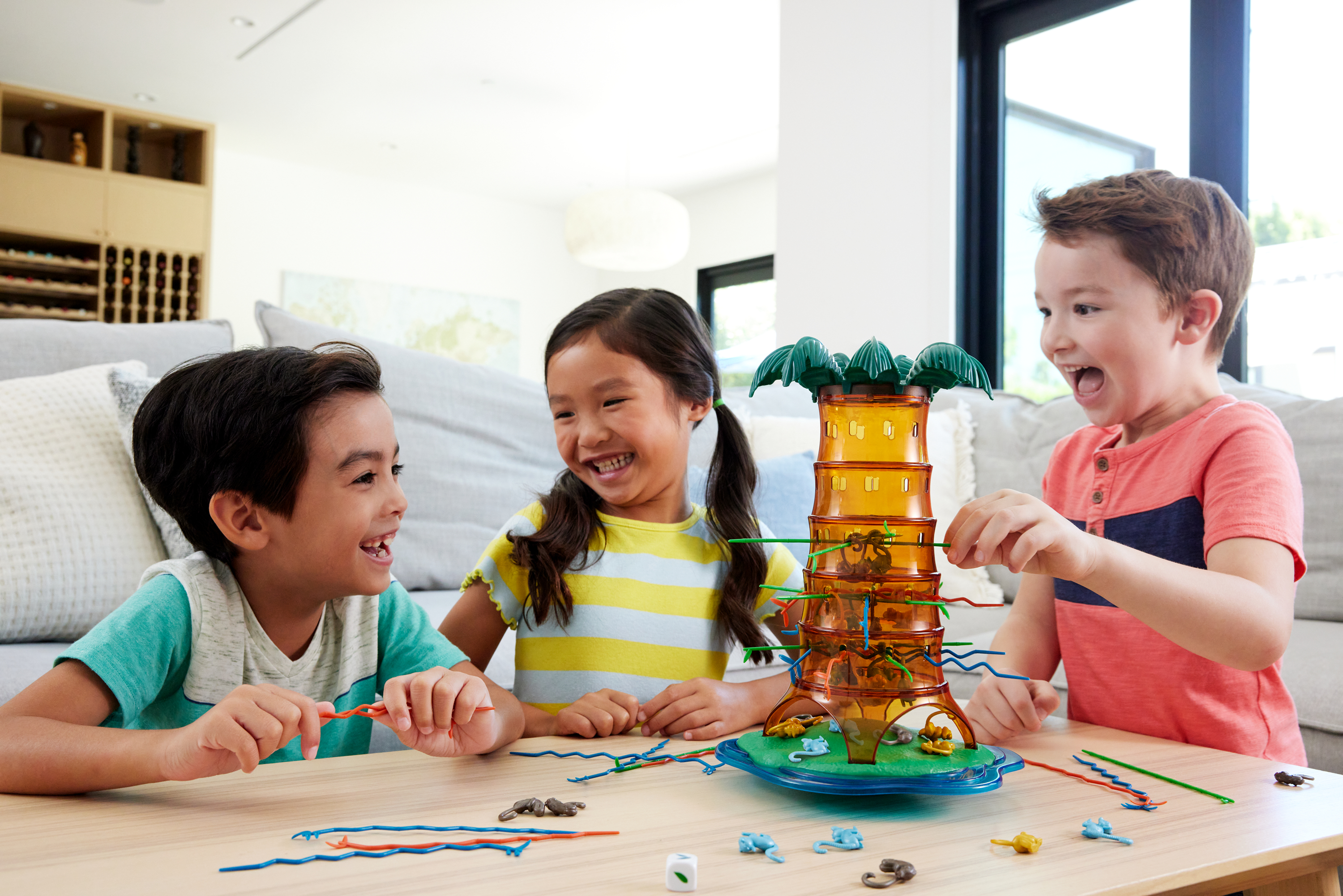 Troje dzieci gra w grę. Gra w wieżę jest na stole. Wszyscy się uśmiechają i wyglądają na podekscytowanych.