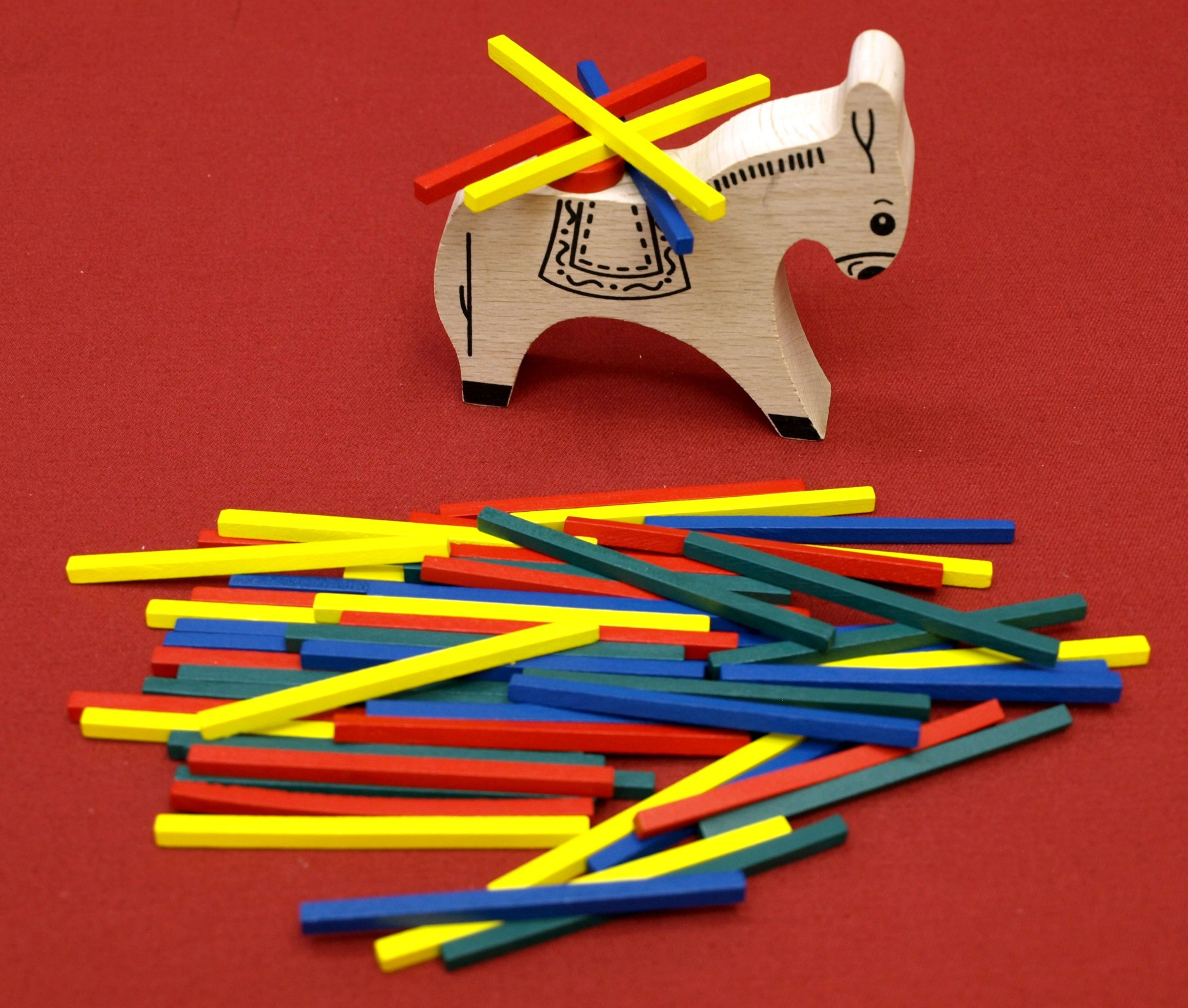 Hölzernes Eselspielzeug mit bunten Stäben auf roter Oberfläche. Stäbe sind gelb, rot, blau und grün.