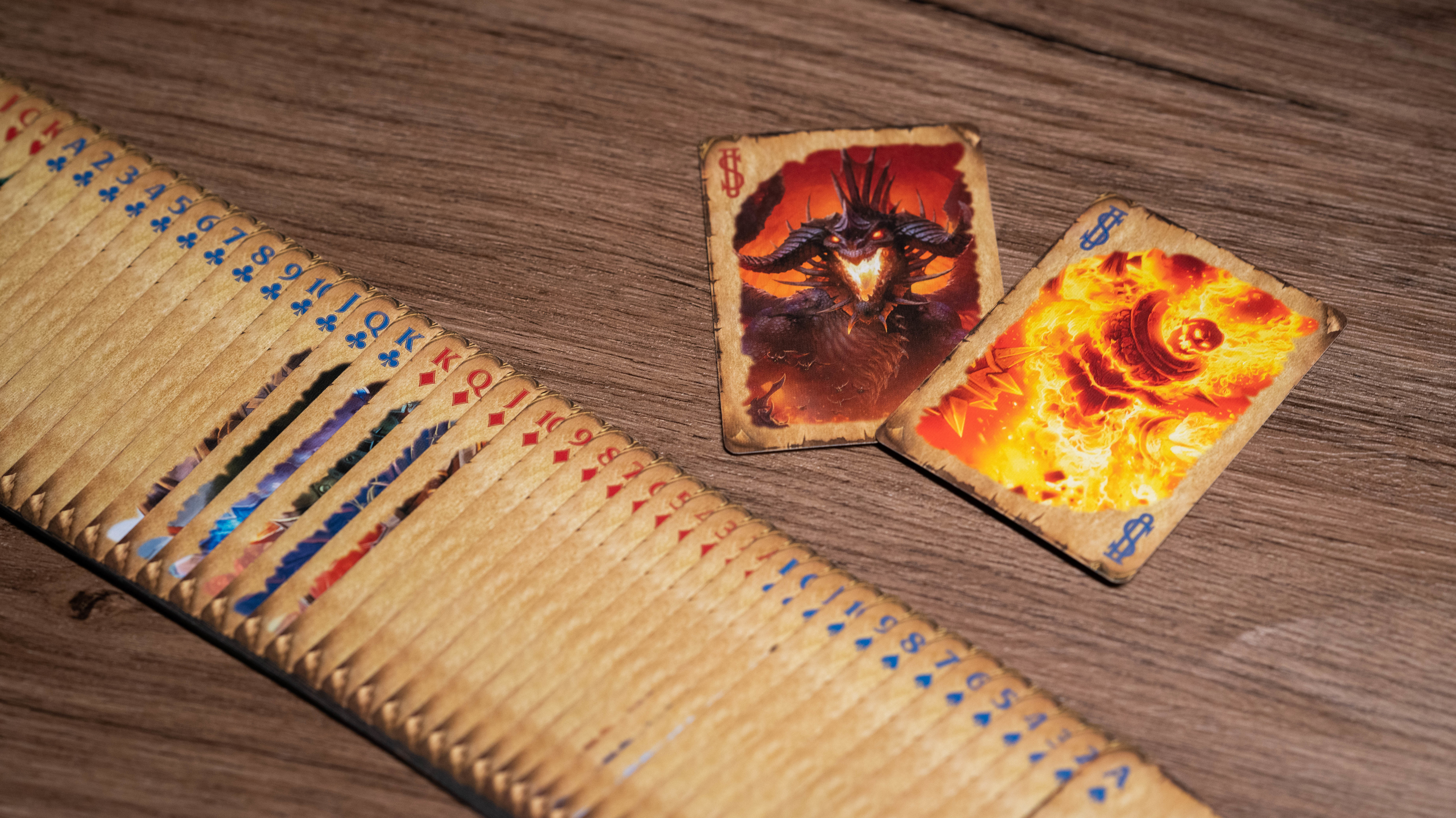Ein Kartenspiel mit zwei offenen Karten, die einen Dämon und Feuer darstellen, auf einer Holzoberfläche.