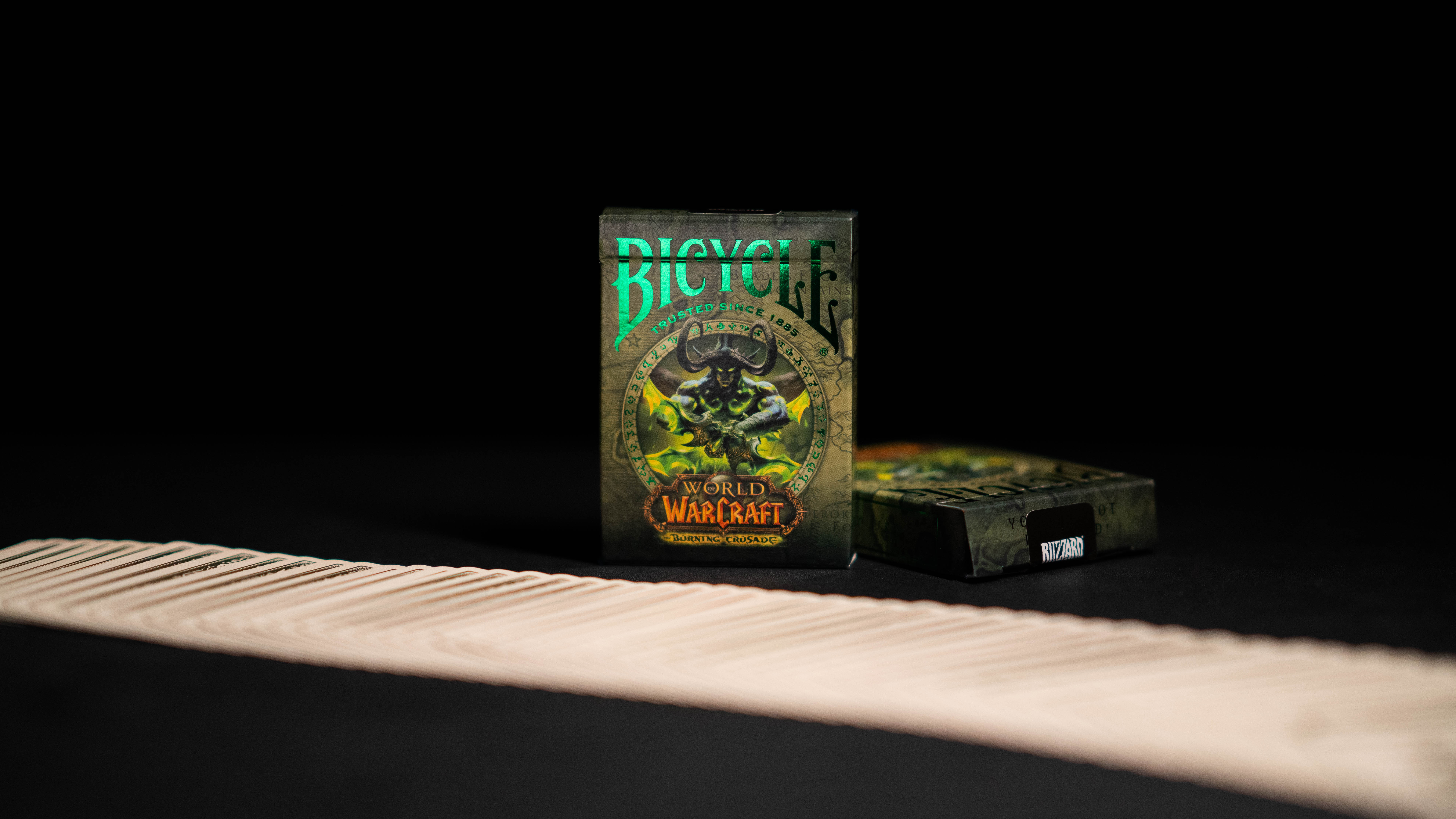 Ein Kartenspiel von World of Warcraft mit einer grün-schwarzen Bicycle-Box und gefächerten Karten auf schwarzem Untergrund.