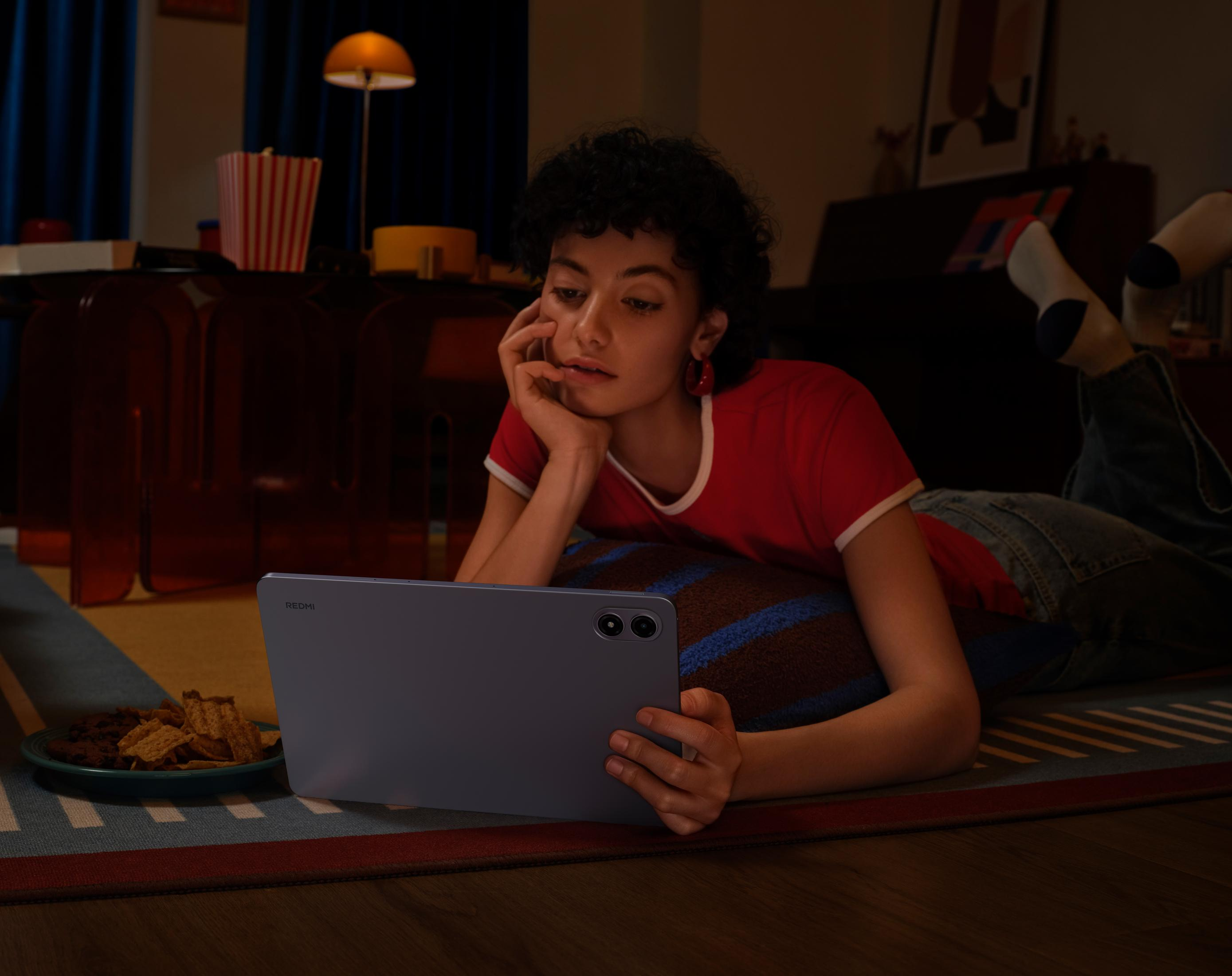 Kobieta leży na dywanie, używając tabletu. Przekąski i popcorn w pobliżu. Ciemne wnętrze.