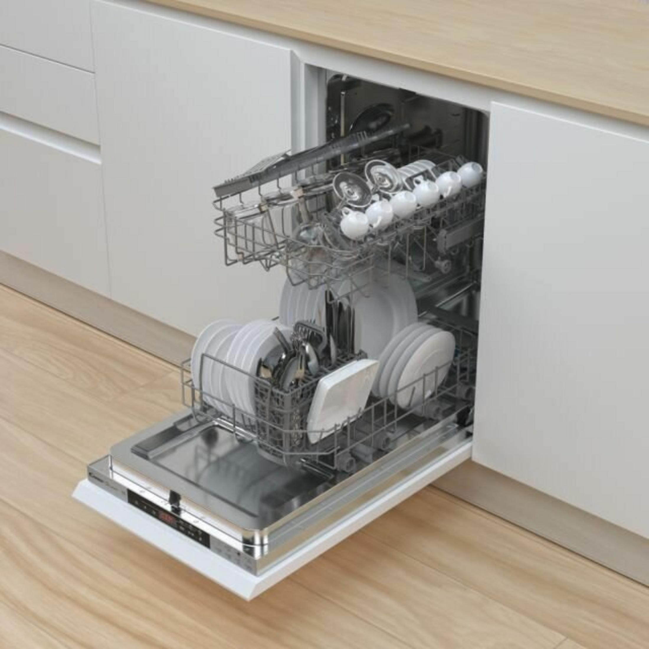Un lavavajillas abierto lleno de platos, vasos y utensilios. El lavavajillas está en un mueble de cocina blanco.