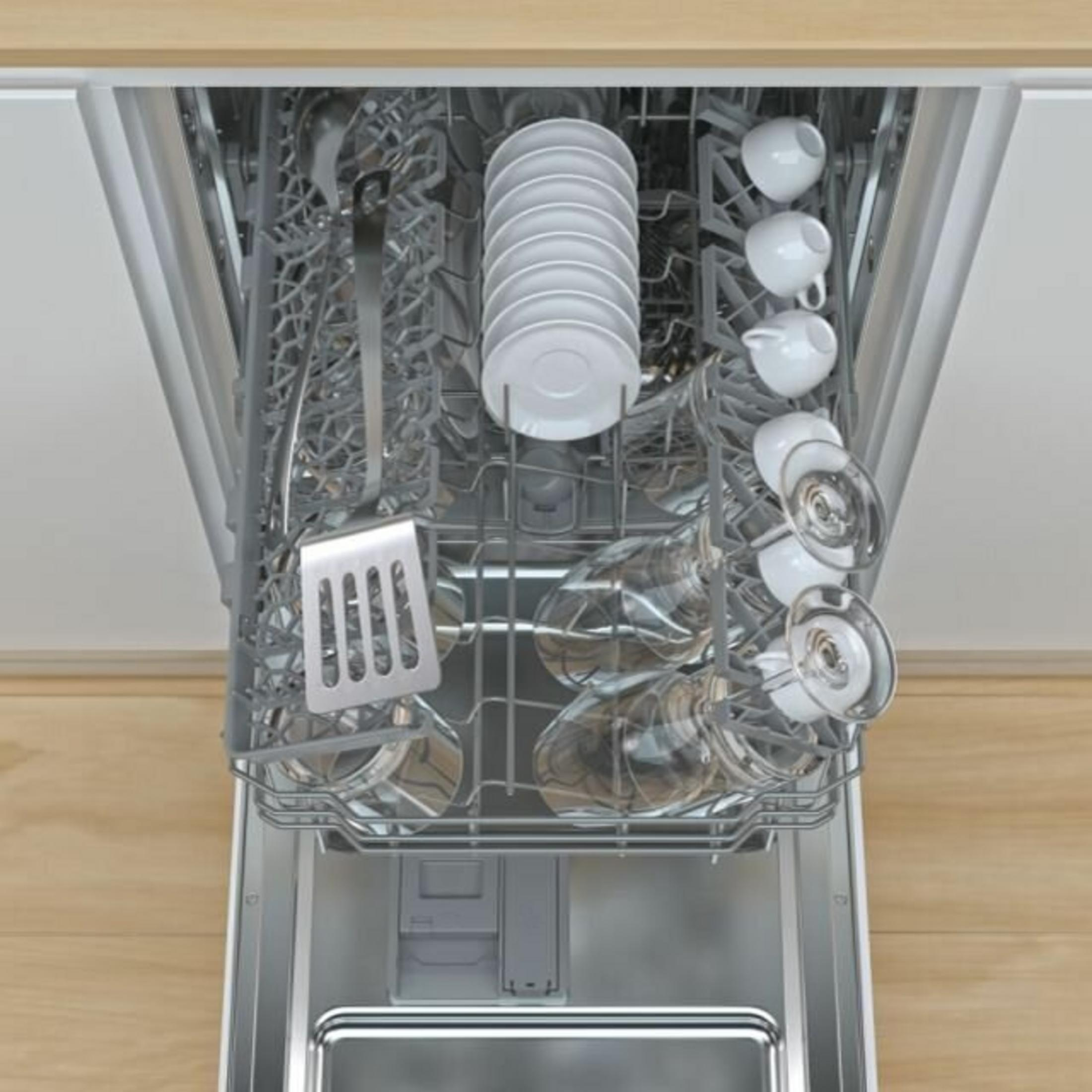 El interior de un lavavajillas está lleno de platos. Platos blancos, vasos, tazas y utensilios están dispuestos para limpiar.