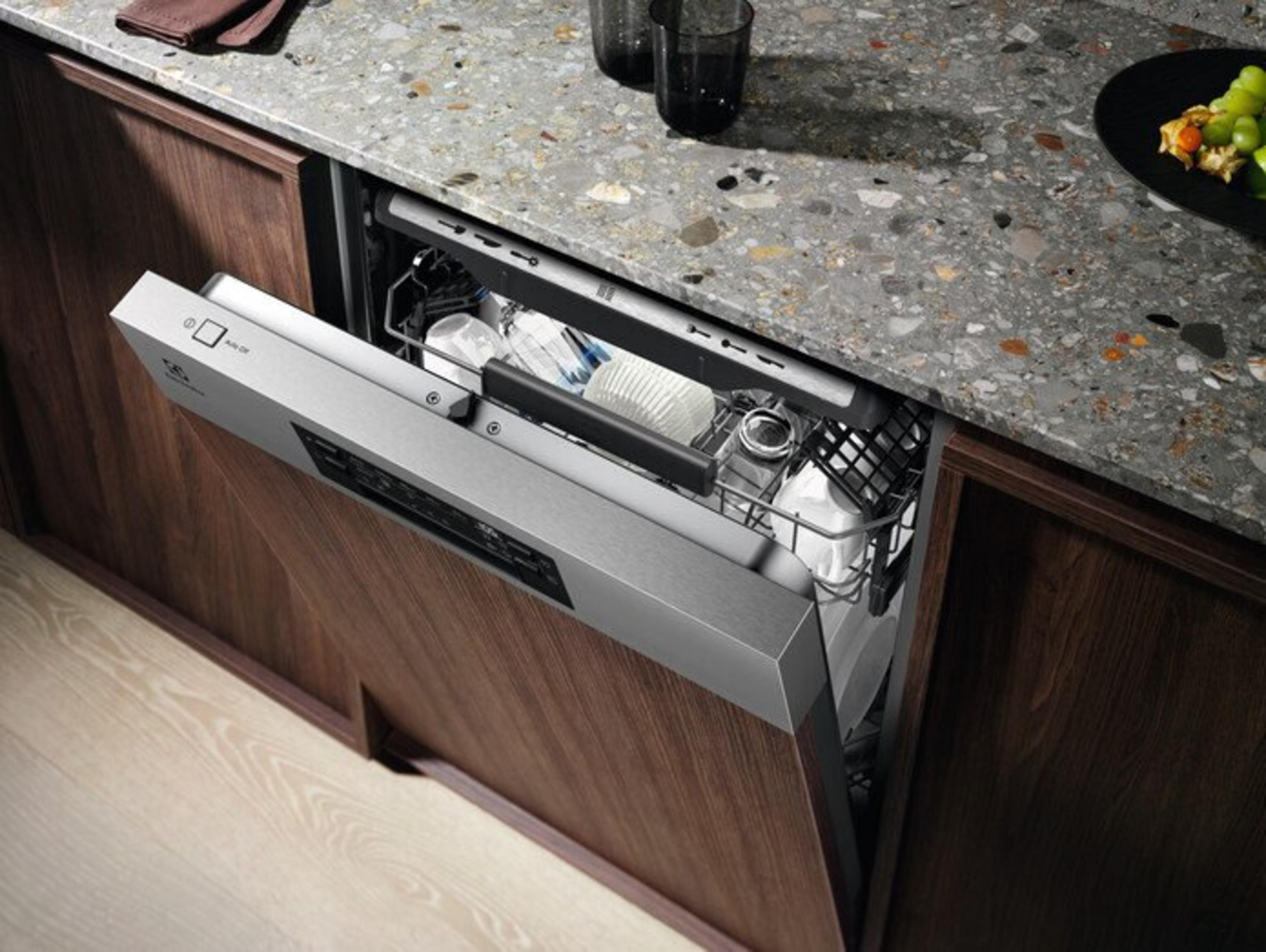 Lavastoviglie aperta con piatti all'interno. Cucina a incasso con mobili in legno e piano in granito.