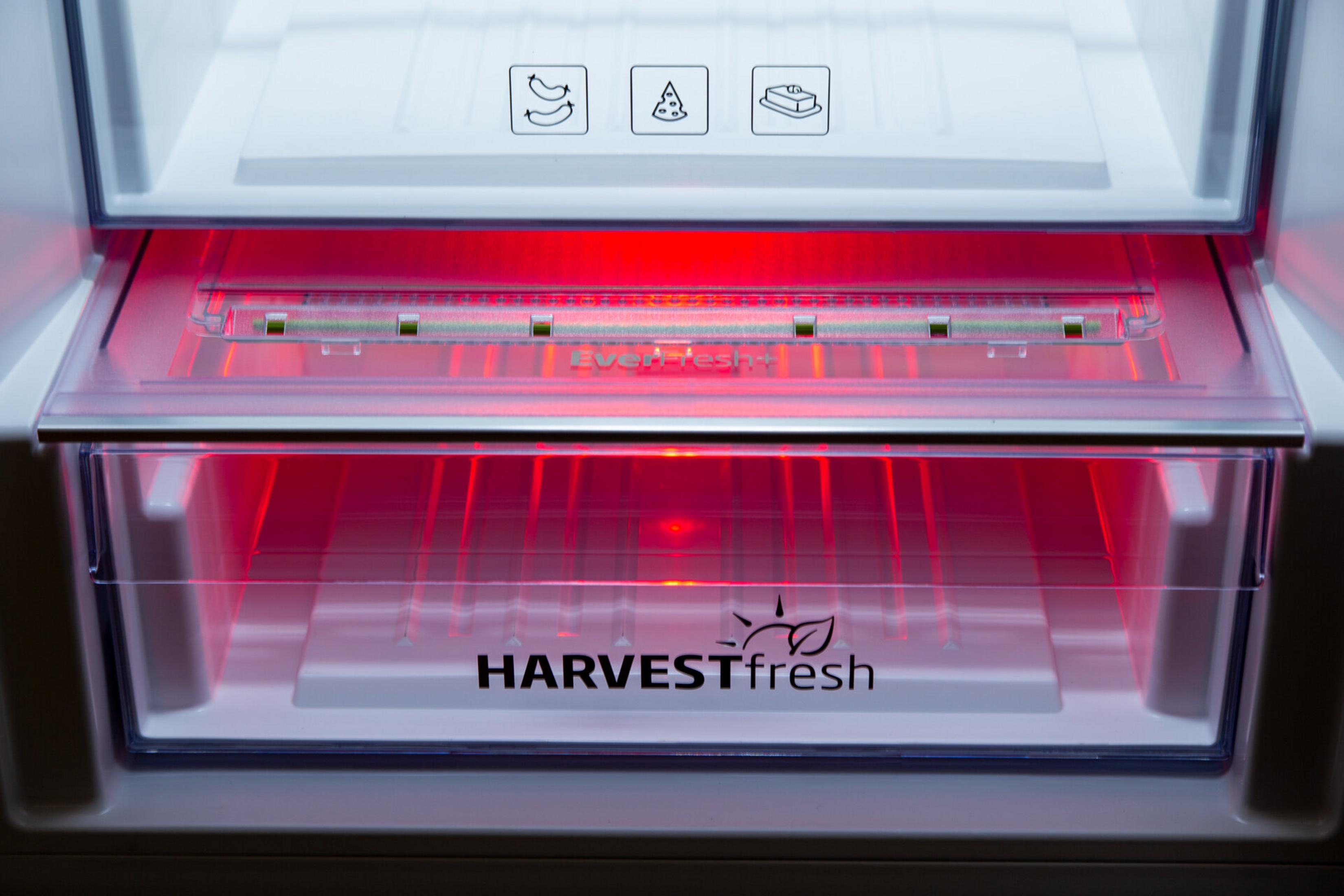 Wnętrze lodówki z czerwonymi światłami. Dolna szuflada z napisem HARVESTfresh. Widoczne ikony kiełbasy, pizzy i masła.