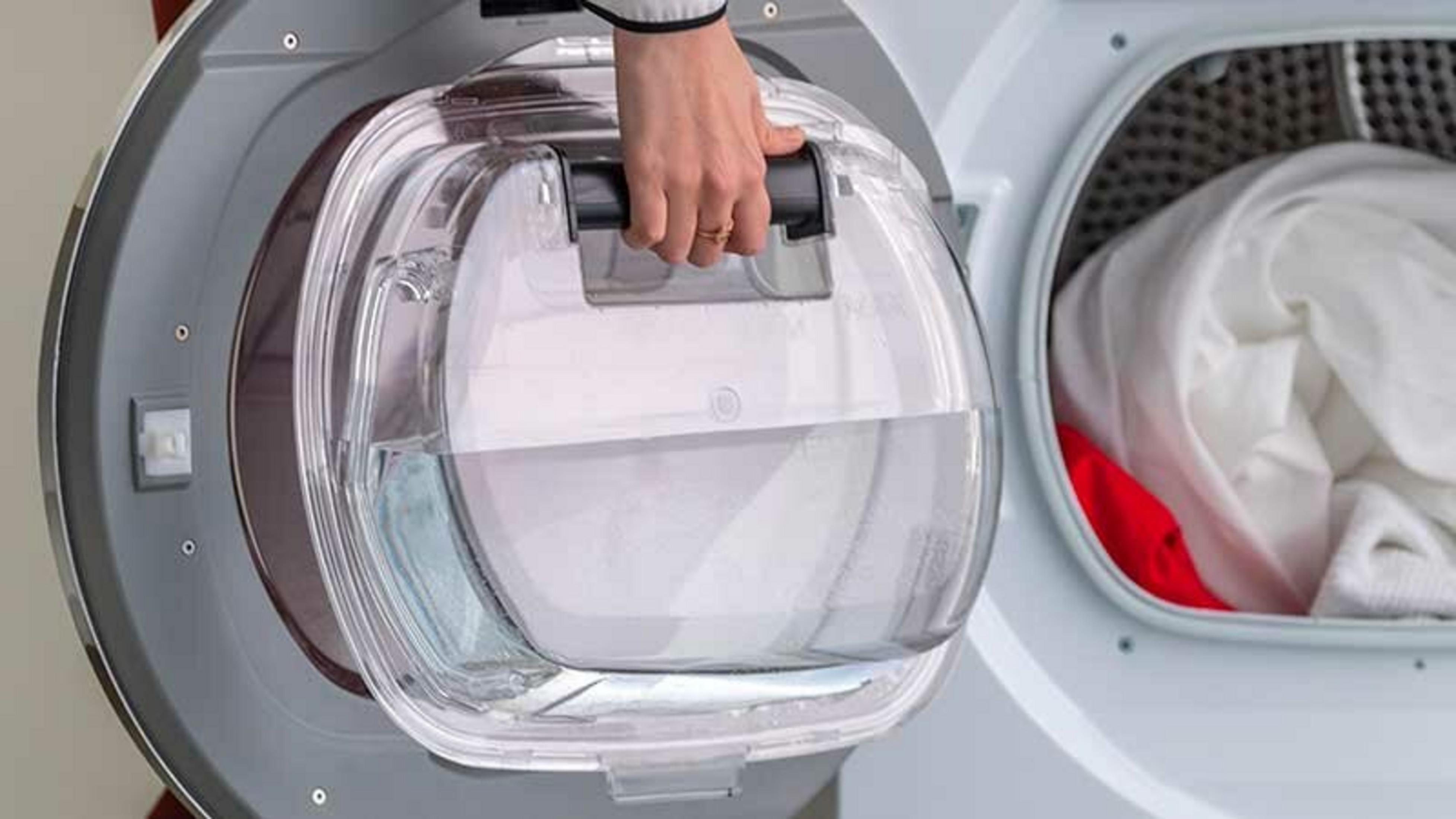 Una persona apre il contenitore dell'acqua di una lavatrice. È parzialmente pieno d'acqua. All'interno della macchina è visibile biancheria bianca.