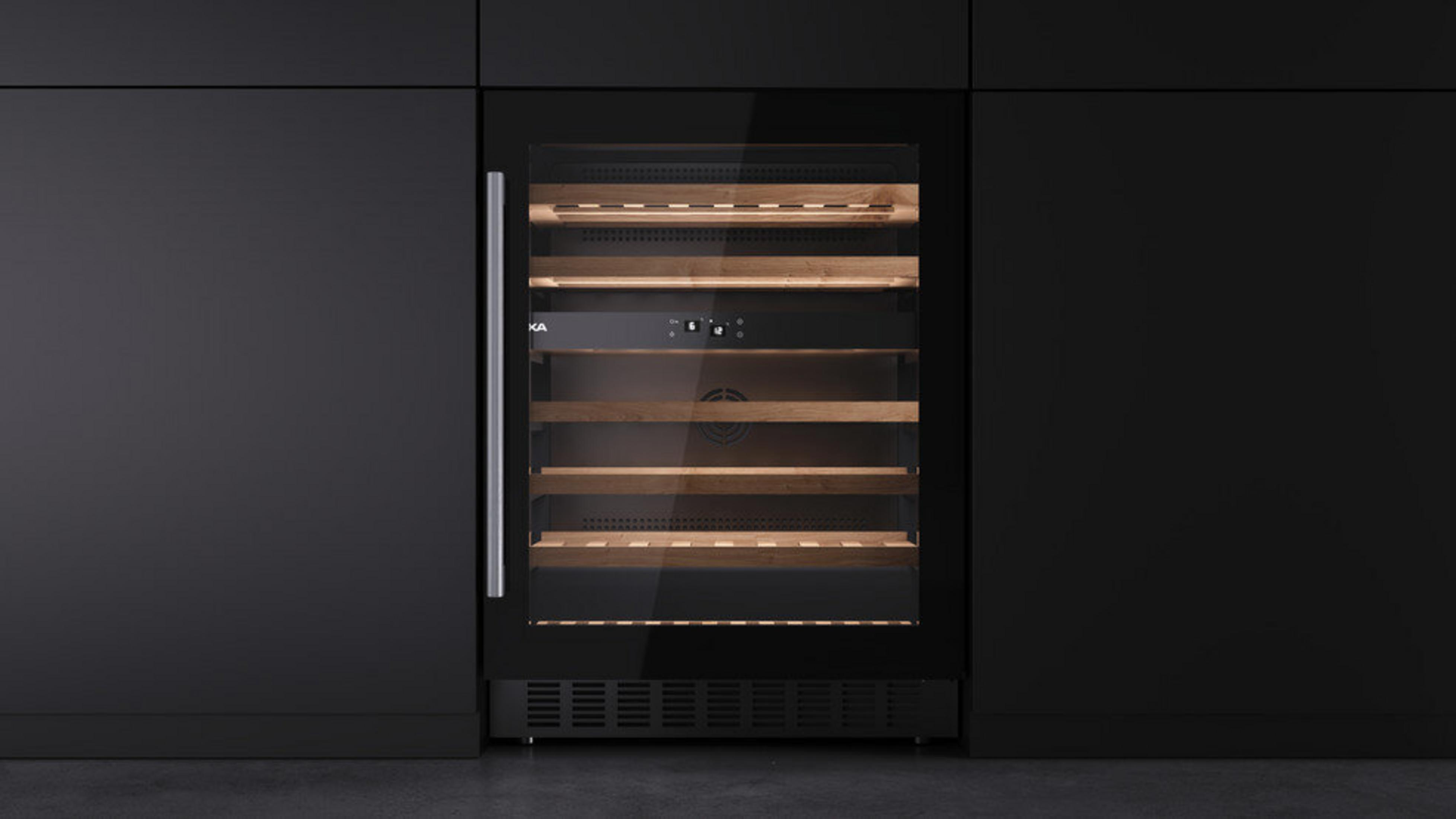 Nowoczesna lodówka na wino, wbudowana w czarne szafki. Ma drewniane półki i szklane drzwi ze srebrnym uchwytem.