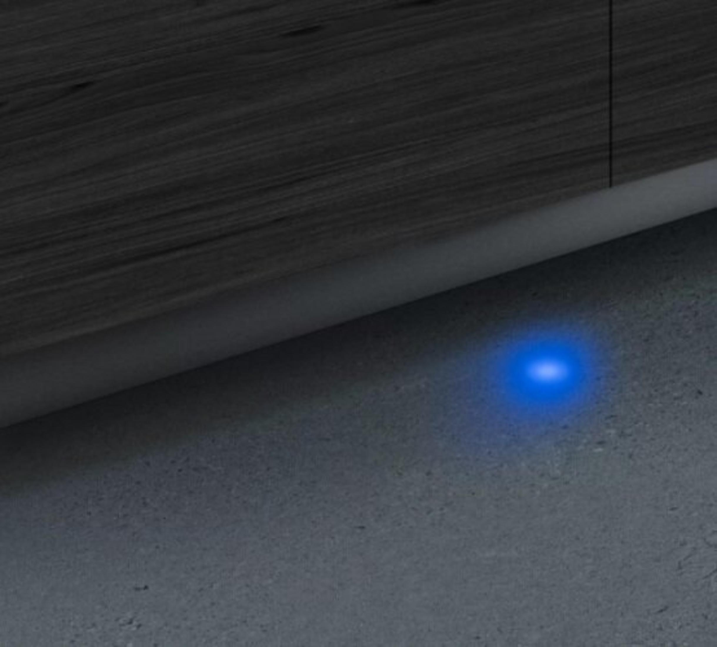 Vista de cerca de una luz azul sobre una superficie gris. Arriba, panel de madera oscura visible.