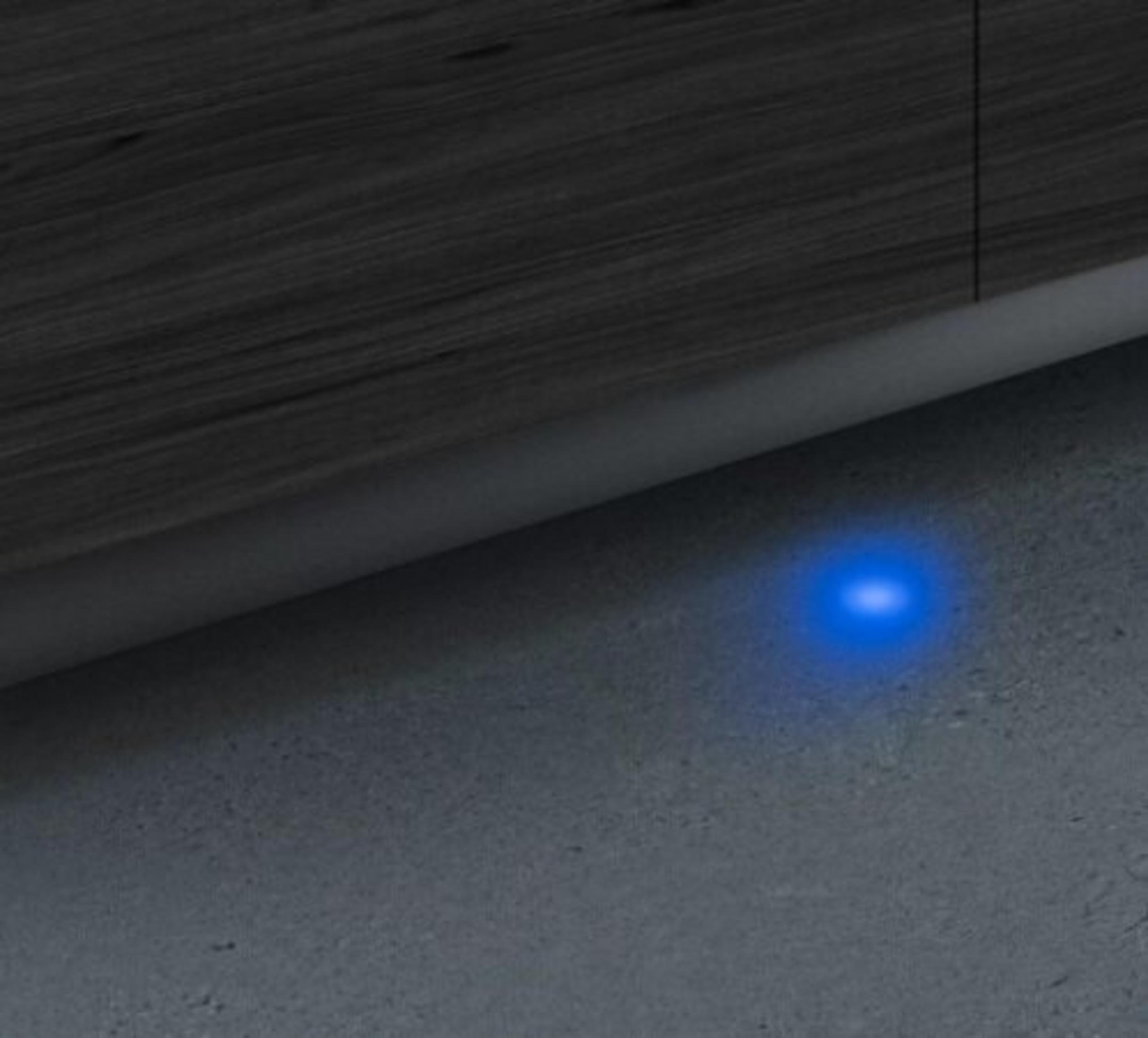 Das Bild zeigt ein blaues Licht auf einer grauen Betonoberfläche mit dunklen Holzpaneelen darüber.