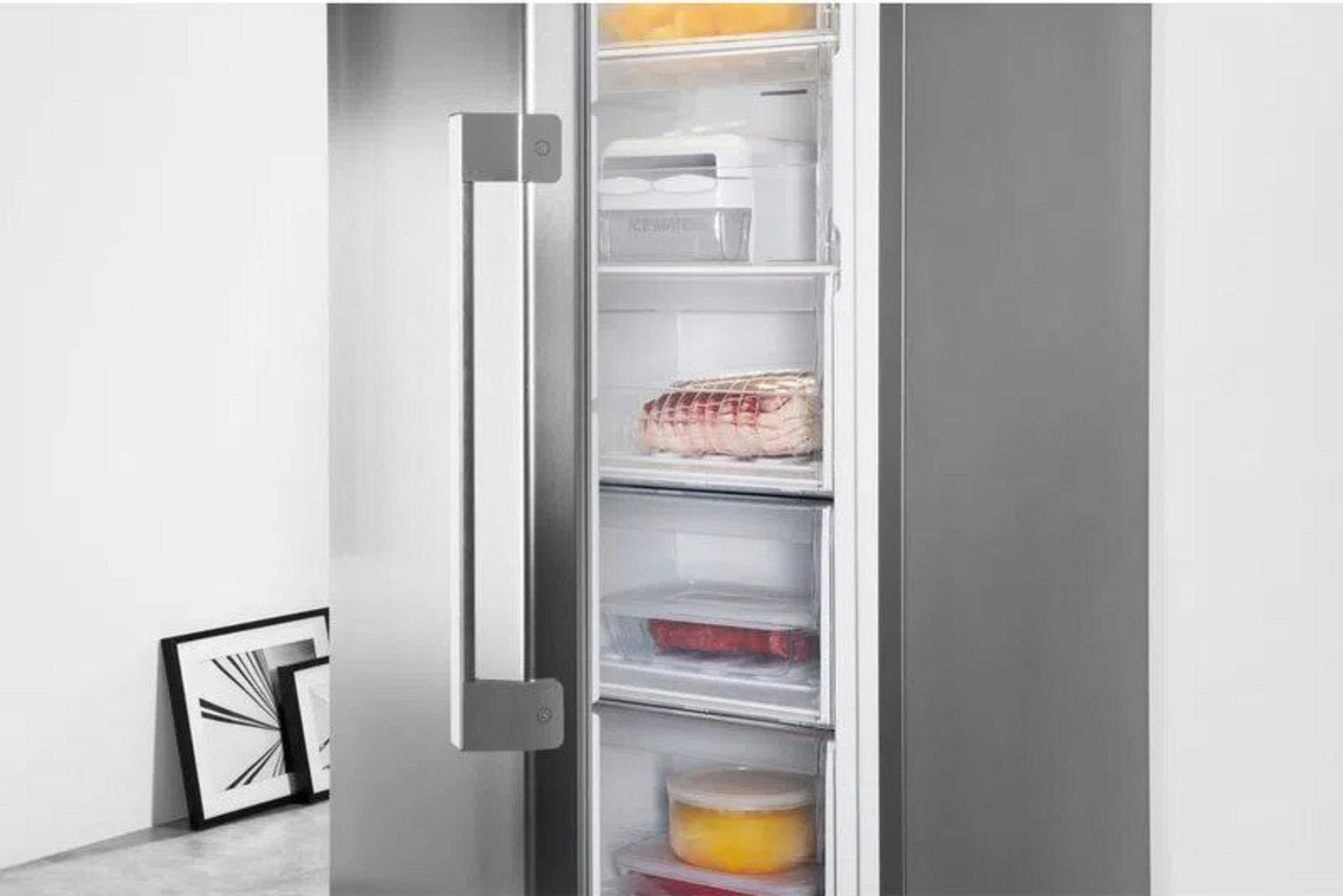 Un refrigerador con la puerta abierta. Dentro hay alimentos. Un marco de imagen está a la izquierda.
