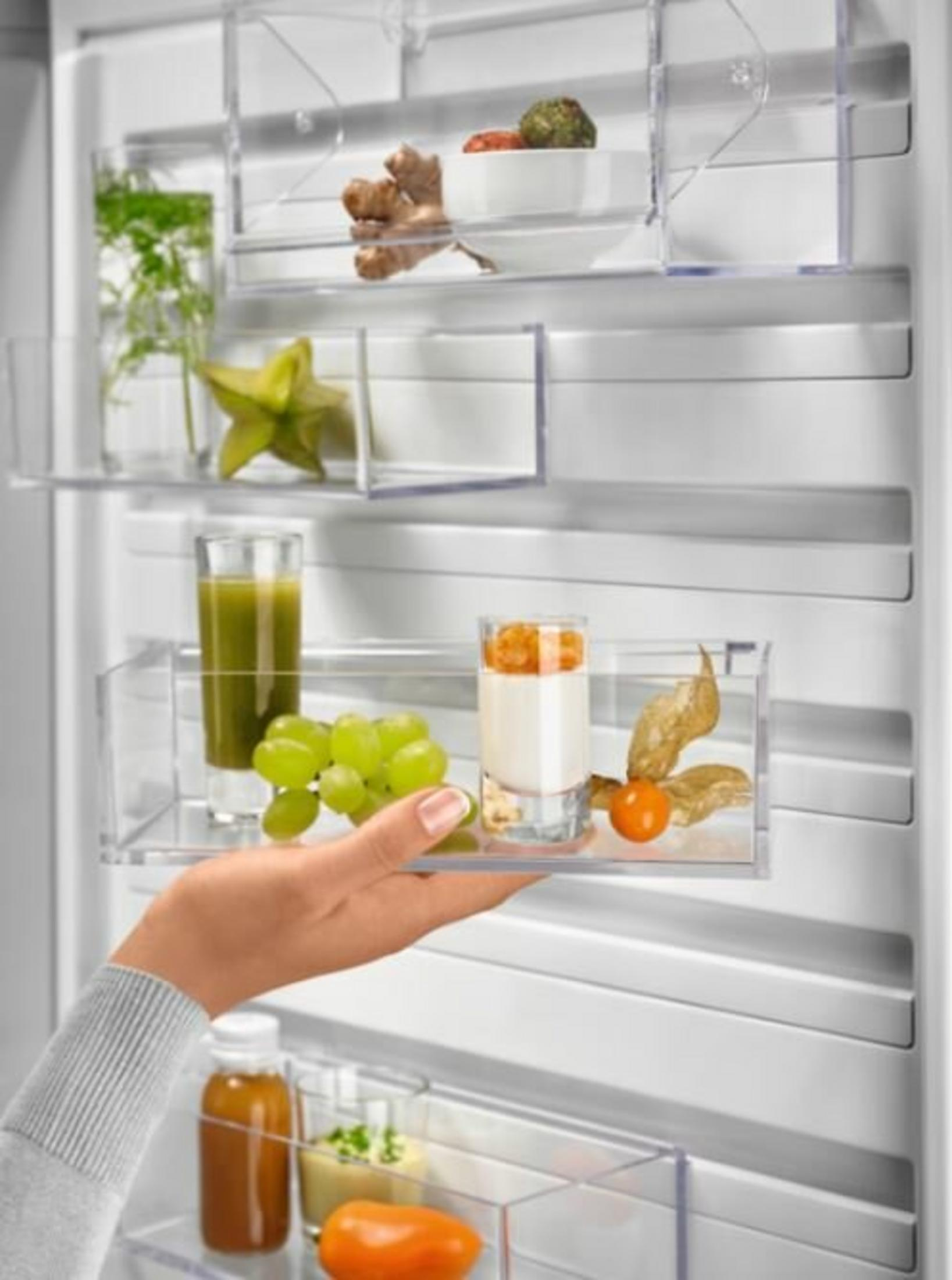 Una mano tiene un vassoio in un frigorifero. Contiene un bicchiere di succo, uva, yogurt e un frutto physalis.