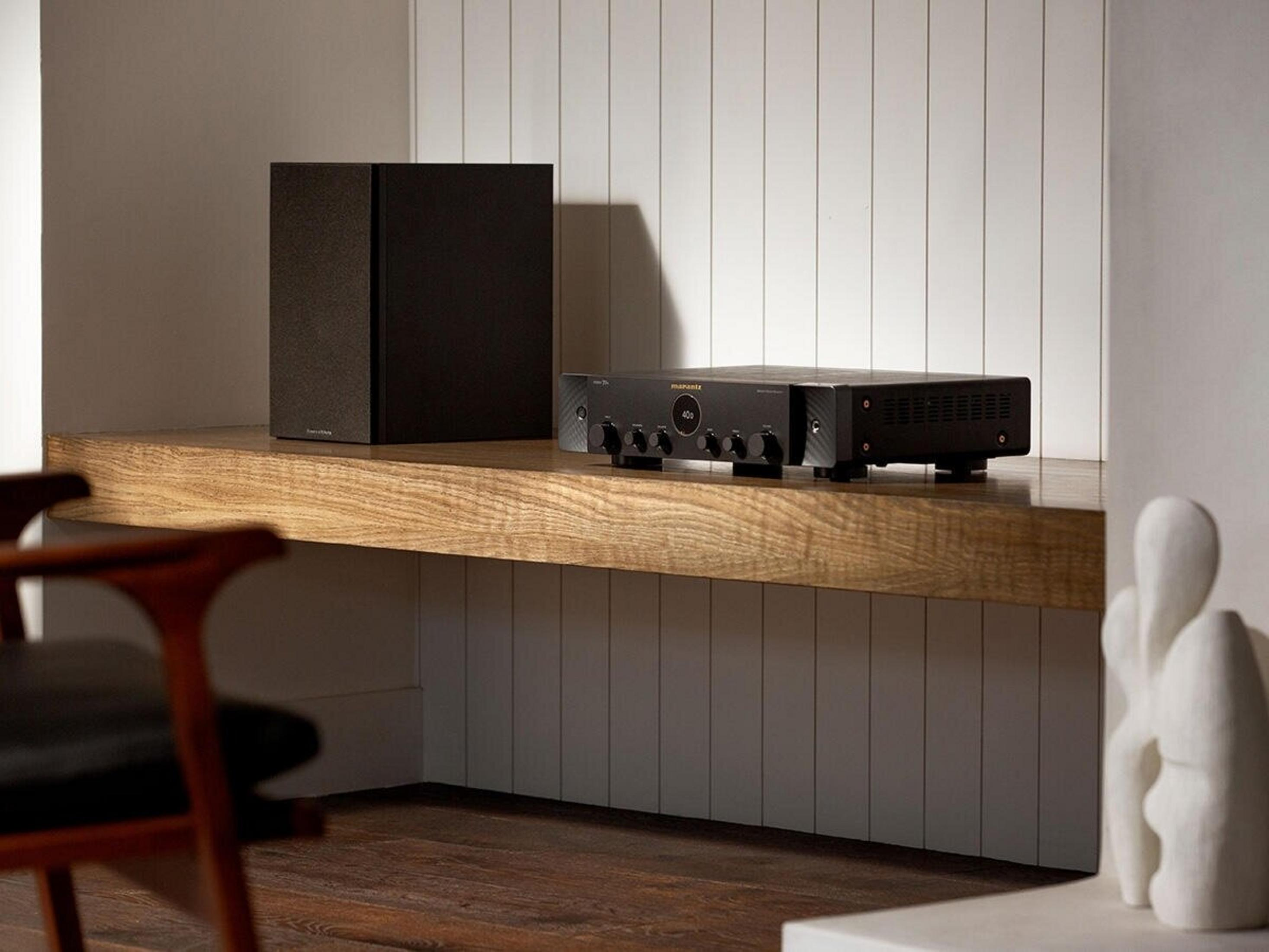 Nowoczesny zestaw audio na drewnianej półce. Zawiera czarny głośnik, odbiornik i białą rzeźbę.