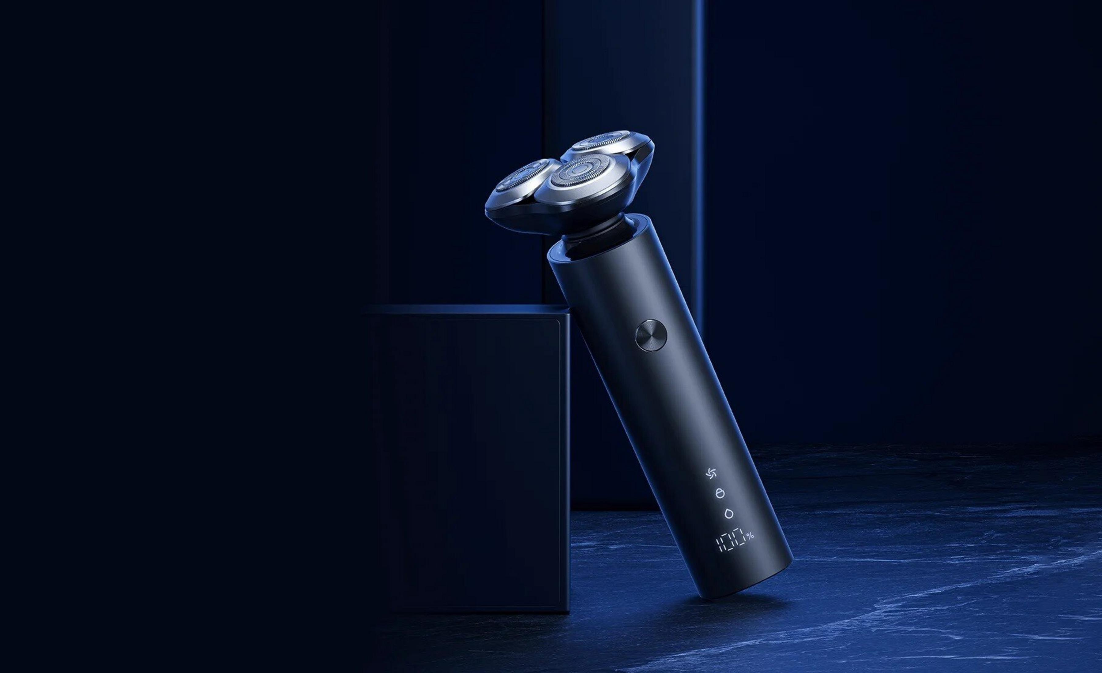 Czarna golarka elektryczna na ciemnoniebieskiej powierzchni. Posiada trzy głowice obrotowe i cyfrowy wyświetlacz pokazujący 100% baterii.