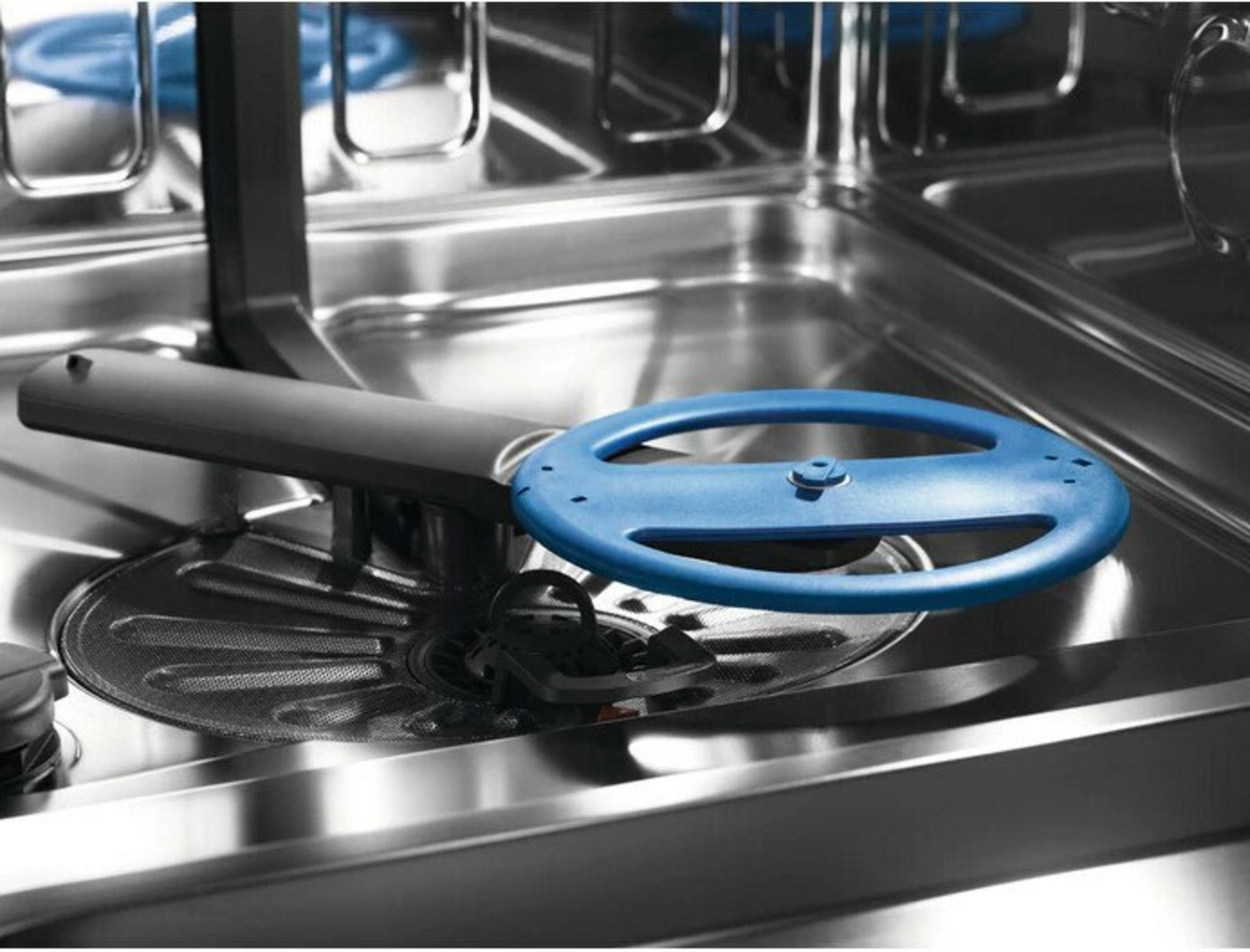 Wewnątrz zmywarki, niebieski okrągły przedmiot jest przymocowany do czarnego ramienia. Wnętrze ze stali nierdzewnej.