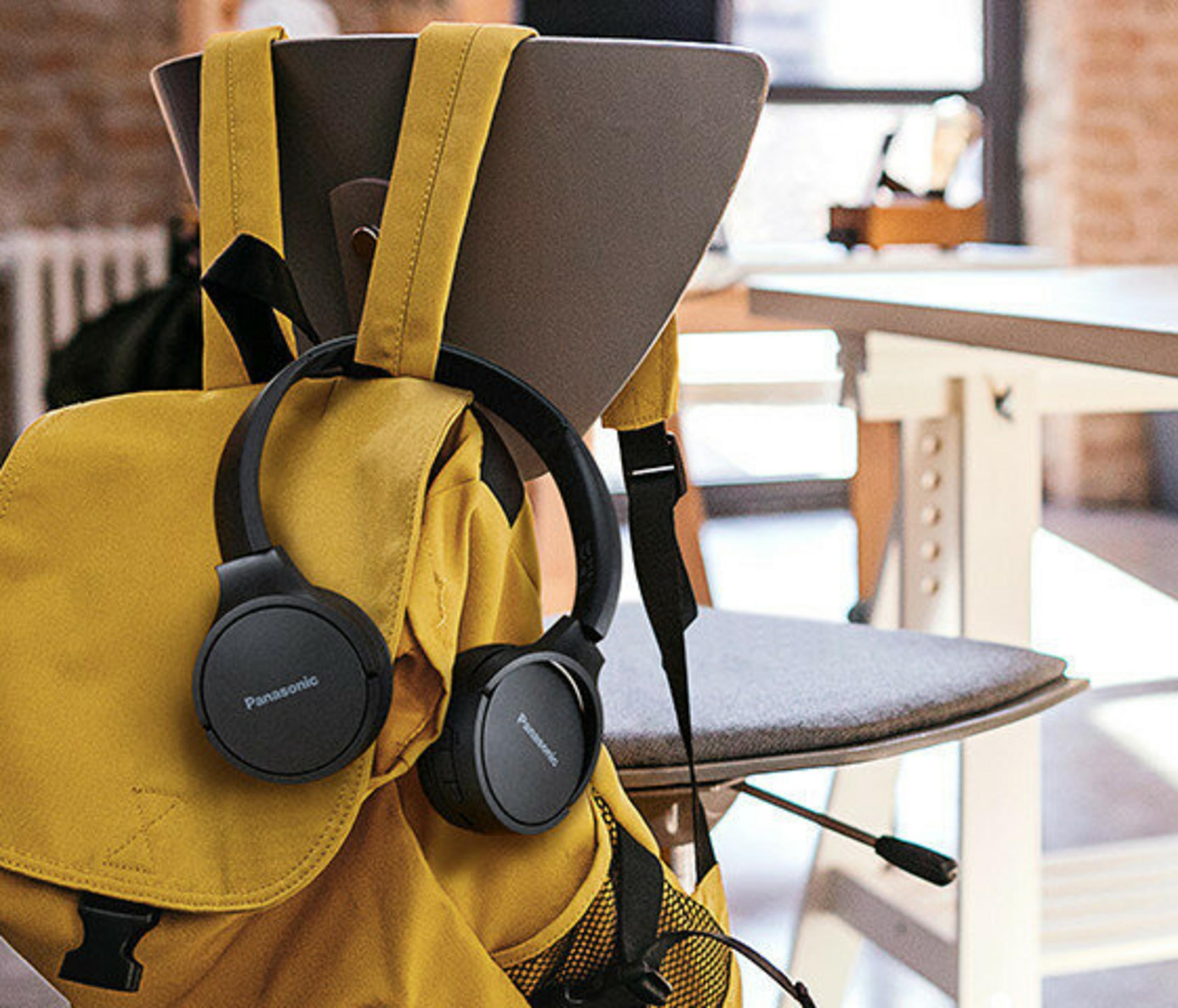 Cuffie Panasonic nere appese a uno zaino giallo su una sedia. Un tavolo sullo sfondo.