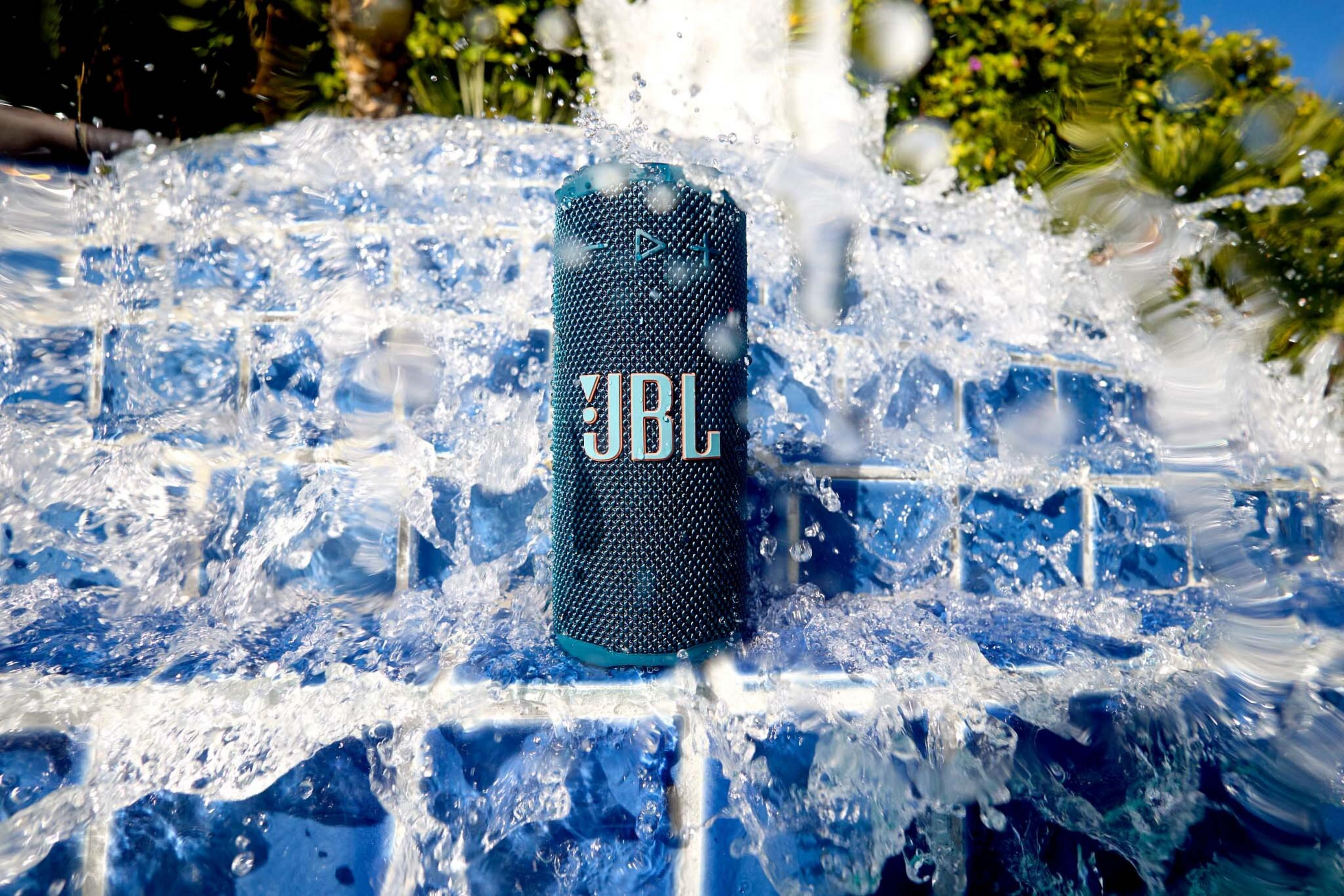 Ein JBL-Lautsprecher im Wasser. Blauer Lautsprecher mit weißem JBL-Schriftzug. Wasser spritzt darum herum.