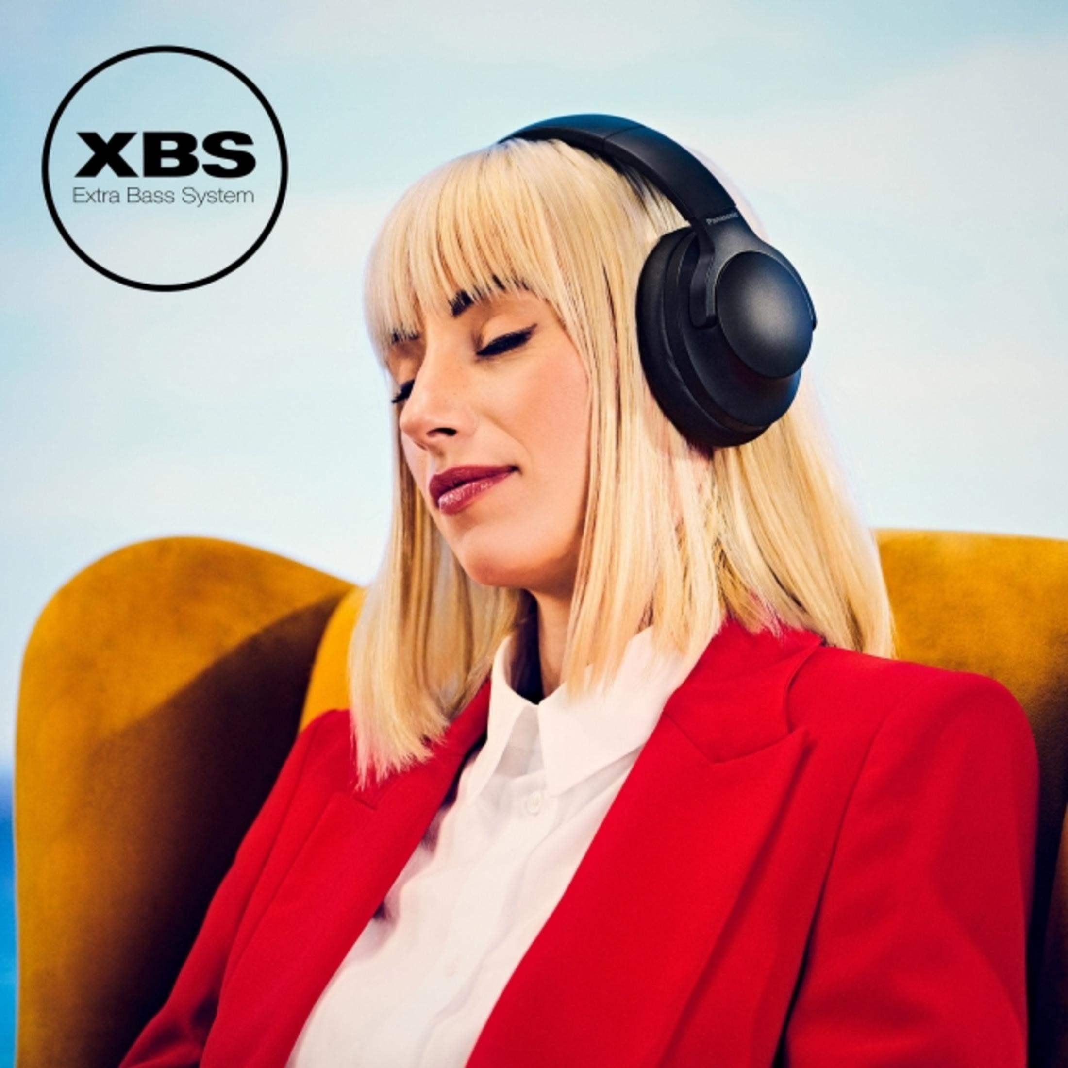 Frau mit Kopfhörern, rotem Blazer und weißem Hemd. XBS-Logo in der oberen linken Ecke. Goldener Stuhl und hellblauer Hintergrund.