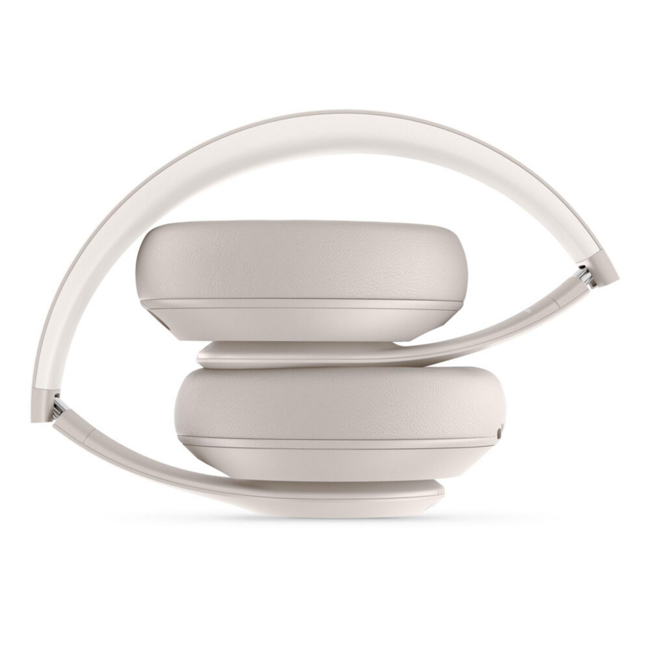 Beige koptelefoon is opgevouwen, met oorschelpen op elkaar. De hoofdband is wit. De achtergrond is wit.