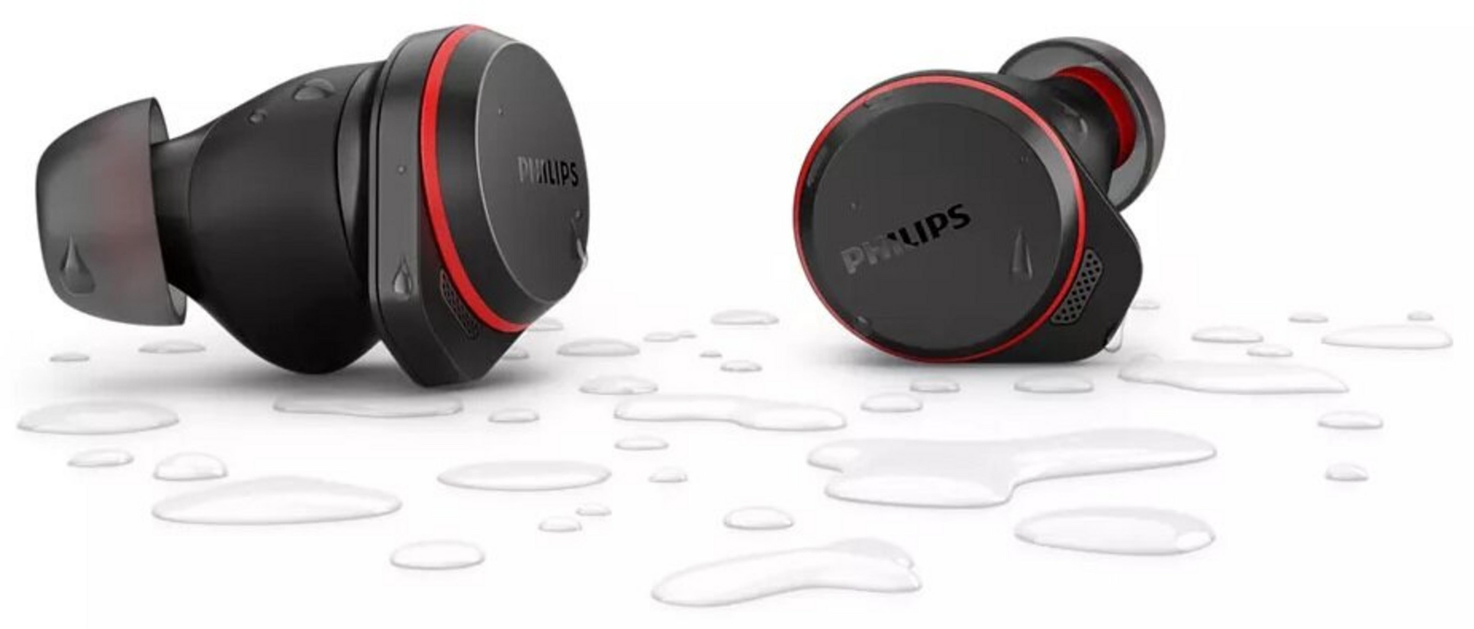 Dwa czarne słuchawki Philips z czerwonymi akcentami na białej powierzchni z kroplami wody. Widoczna nazwa marki.
