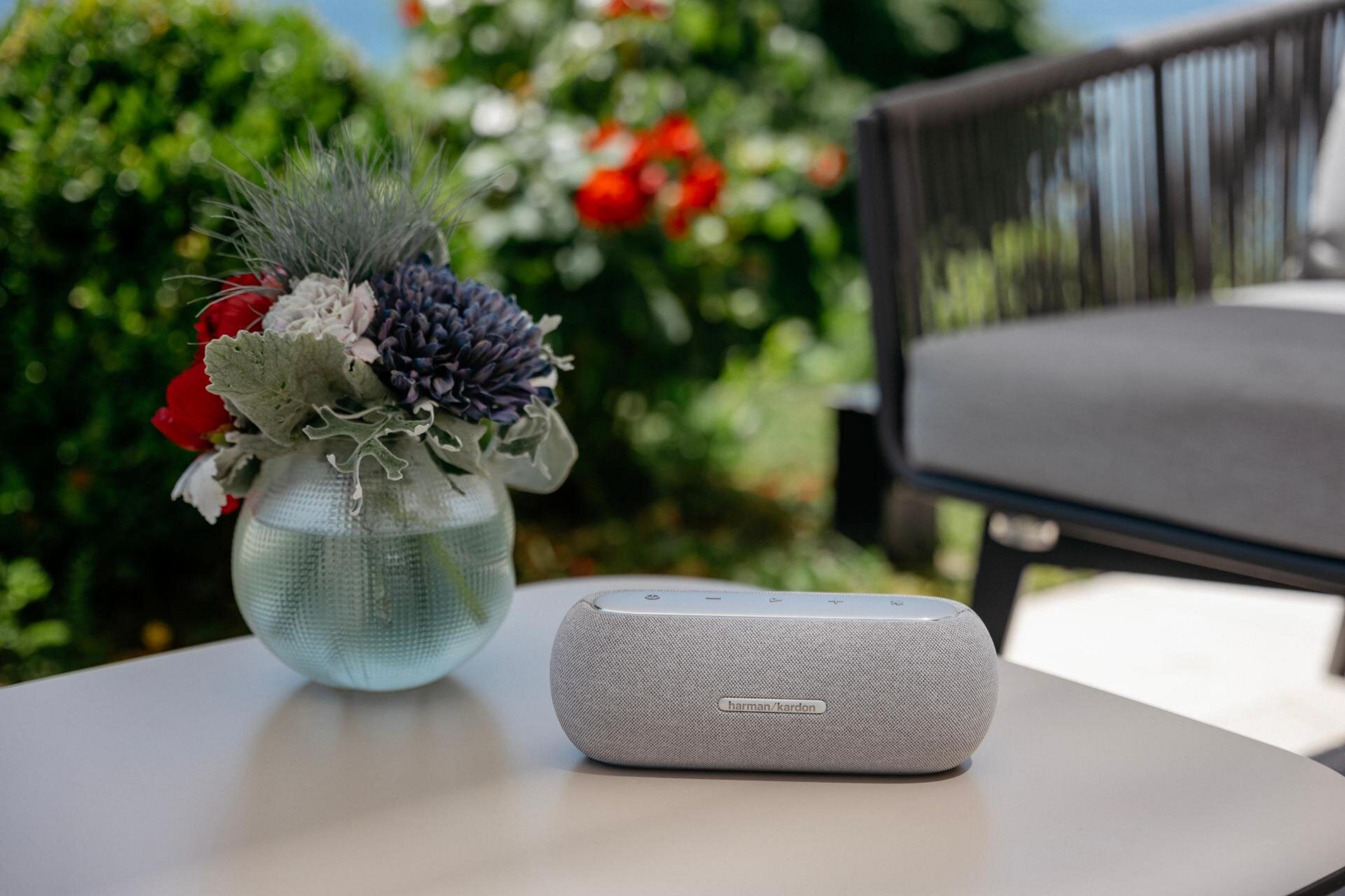 Un altavoz en una mesa junto a un jarrón de flores. Una silla es visible en el fondo.