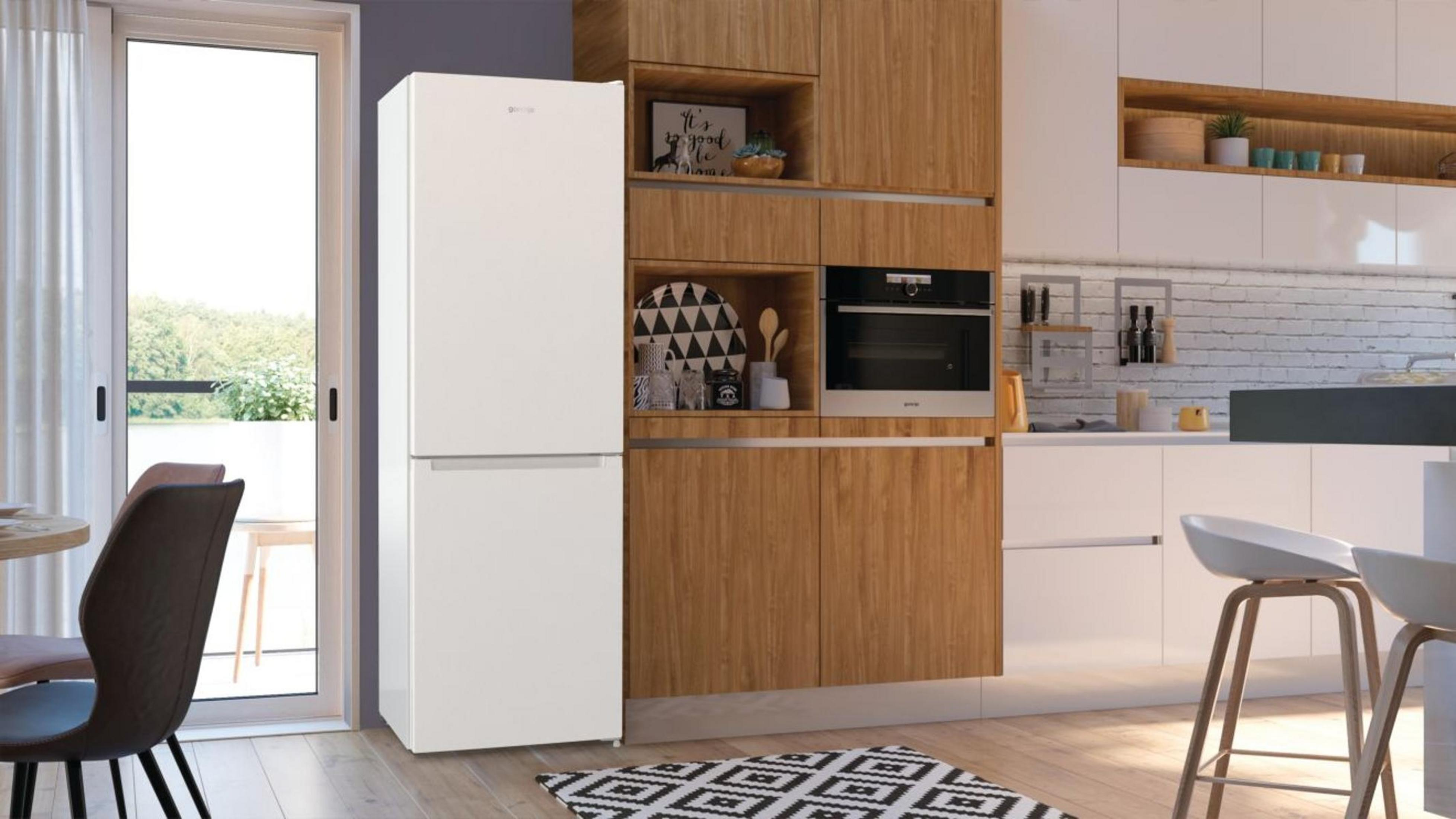 Küche mit weißem Kühlschrank, Holzschränken, Backofen und schwarz-weiß gemustertem Teppich. Eine Tür führt nach draußen.