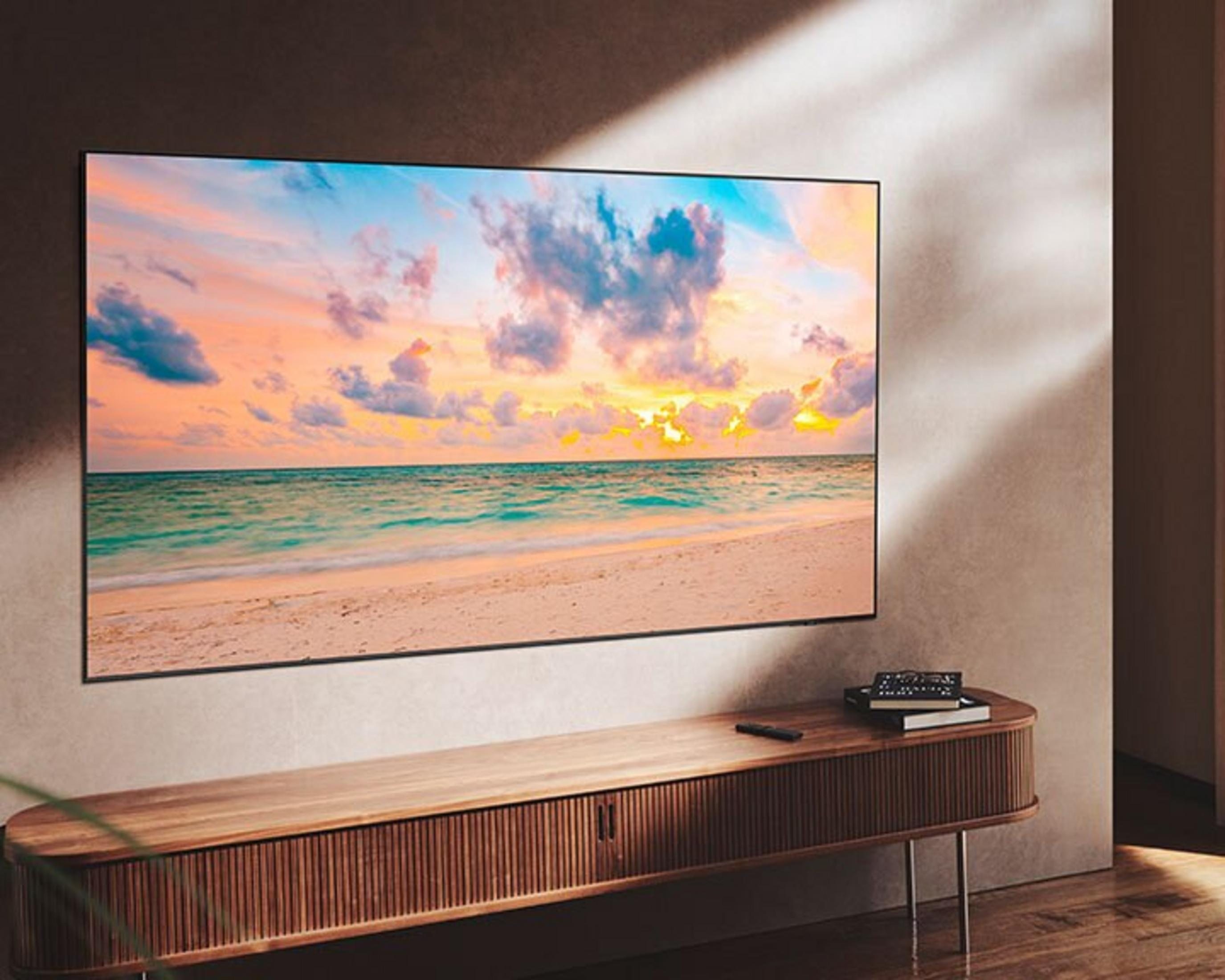 Un televisor muestra una escena de playa. Está encima de un mueble de madera. La pared es marrón claro.