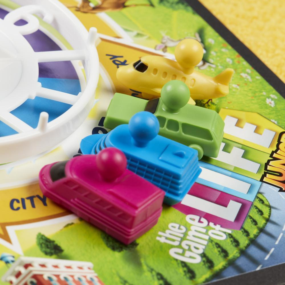 Bunte Spielfiguren auf einem Brett: Flugzeug, Bus, Boot und Zug. Auf dem Brett steht 'Game of Life Junior'.
