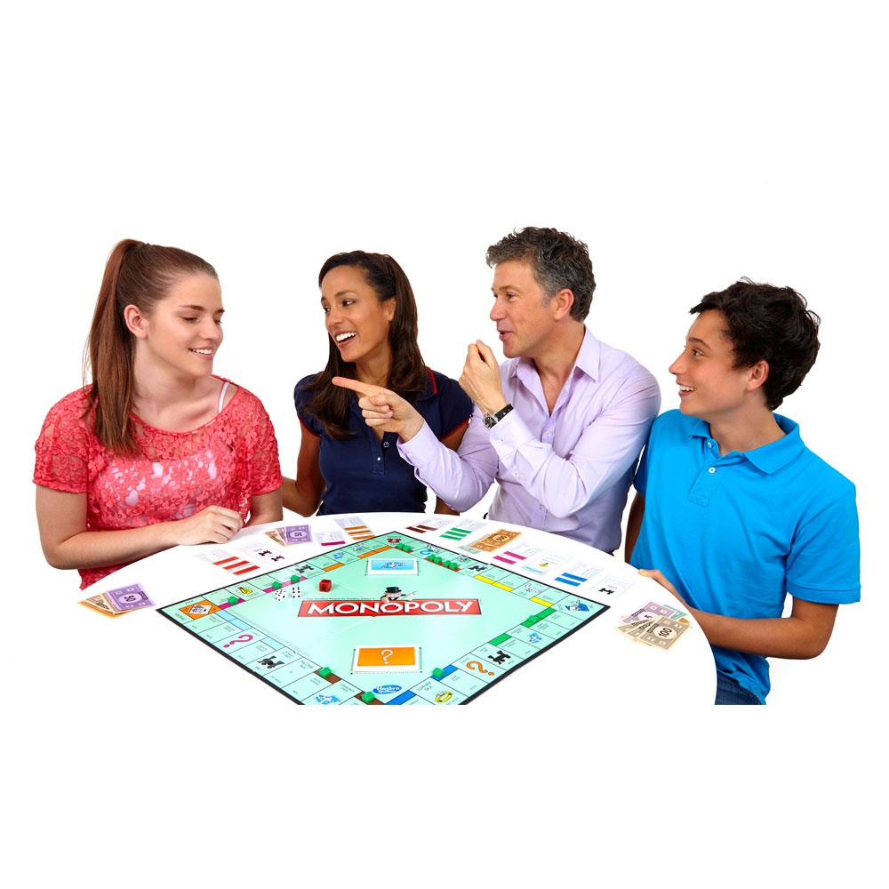 Vier Personen spielen Monopoly. Ein Brettspiel befindet sich in der Mitte mit Würfeln und Spielfiguren. Die Spieler lächeln und interagieren.