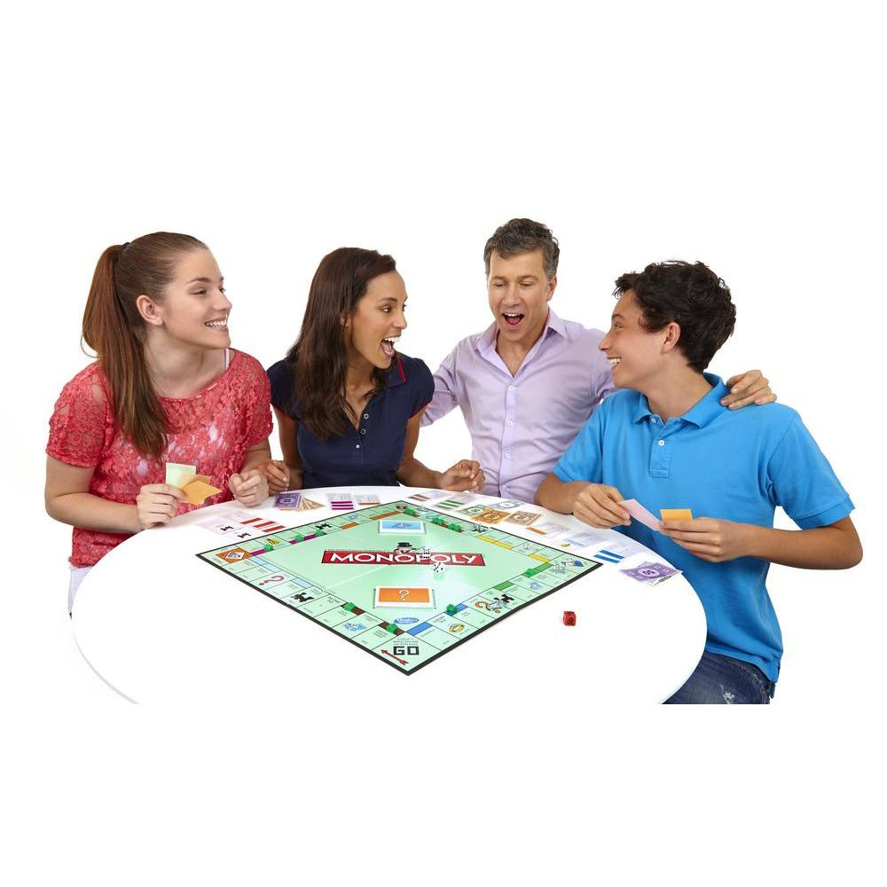 Vier Personen spielen Monopoly an einem weißen Tisch. Sie schauen auf das Spielbrett, die Karten und Würfel mit Begeisterung.
