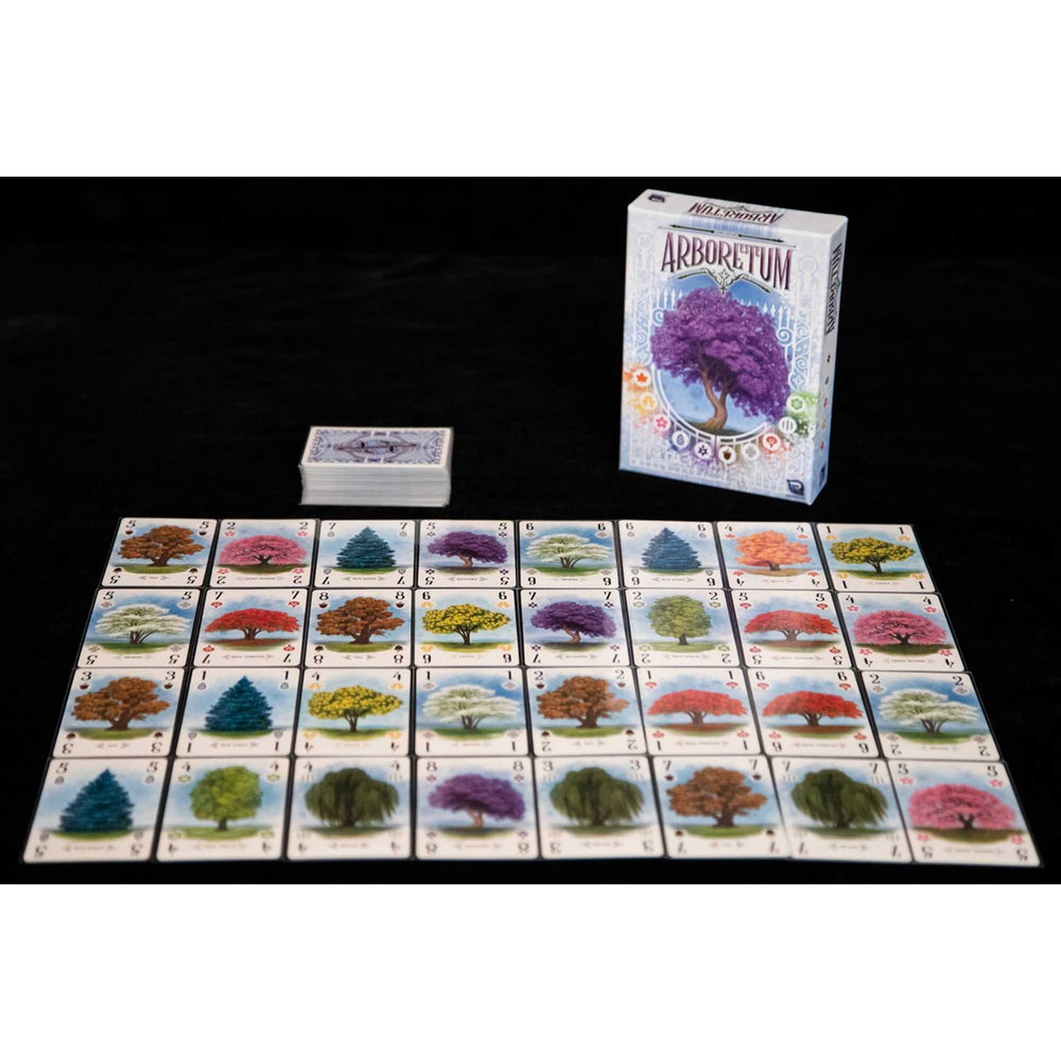 Arboretum-Brettspiel. Karten mit Bäumen sind ausgelegt. Eine Schachtel und ein Kartenstapel liegen auf einer schwarzen Oberfläche.