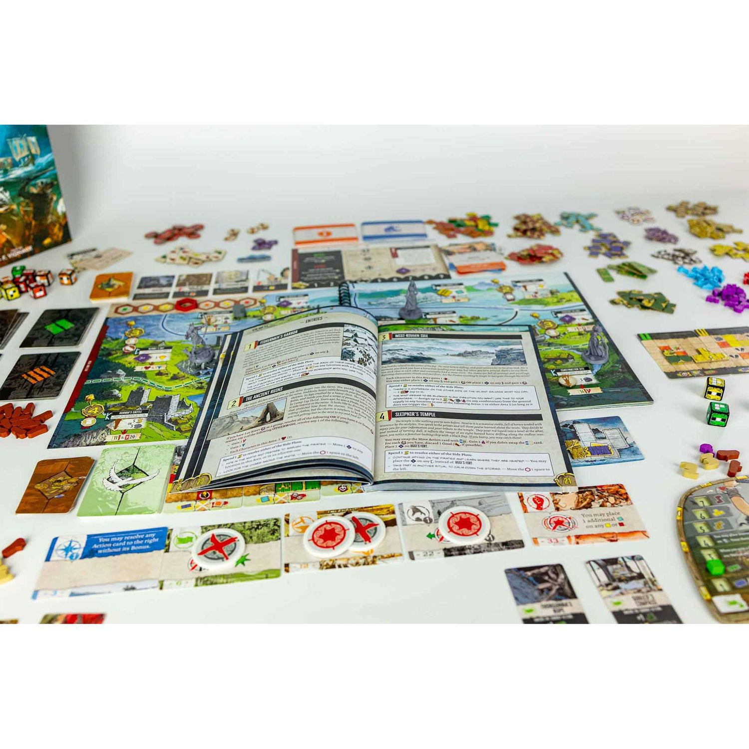 Brettspiel-Setup. Offenes Buch in der Mitte, Karten und Spielsteine verstreut. Würfel und Spielsteine sind auf weißer Oberfläche sichtbar.