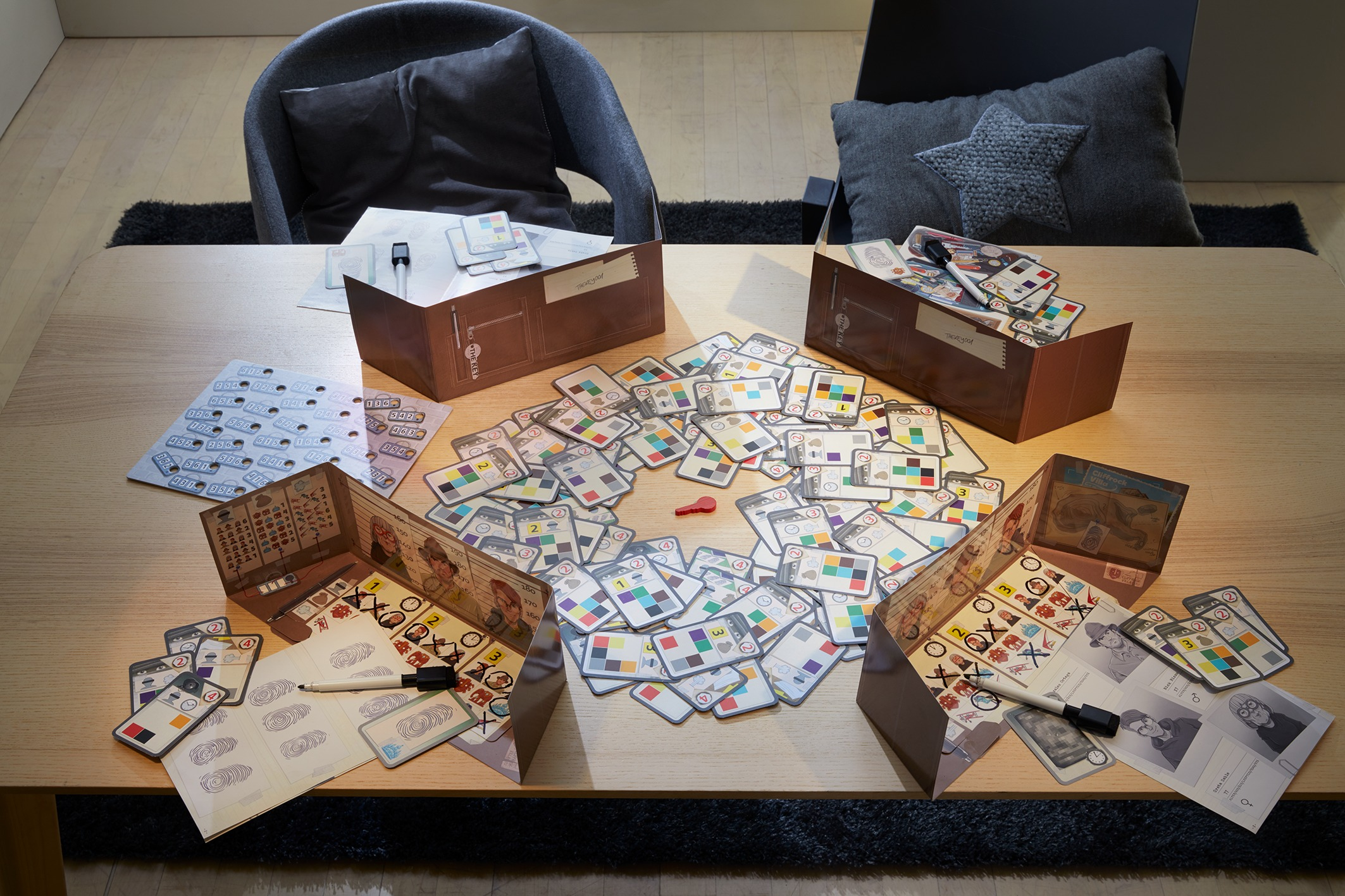 Ein Brettspiel auf einem Holztisch. Karten mit Farben und Zahlen sind um Kartons und Broschüren verstreut.