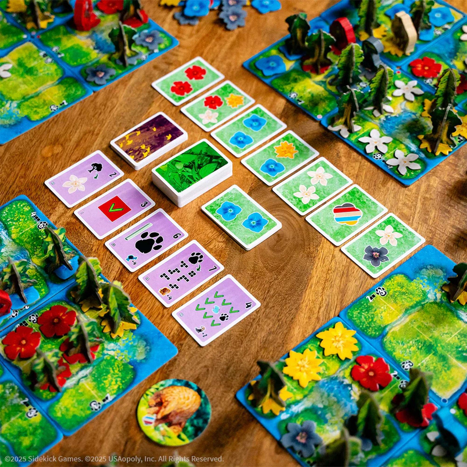 Ein Brettspiel wird mit Karten und Spielbrettern mit Blumen, Bäumen und Tierpfoten auf einer Holzoberfläche angezeigt.