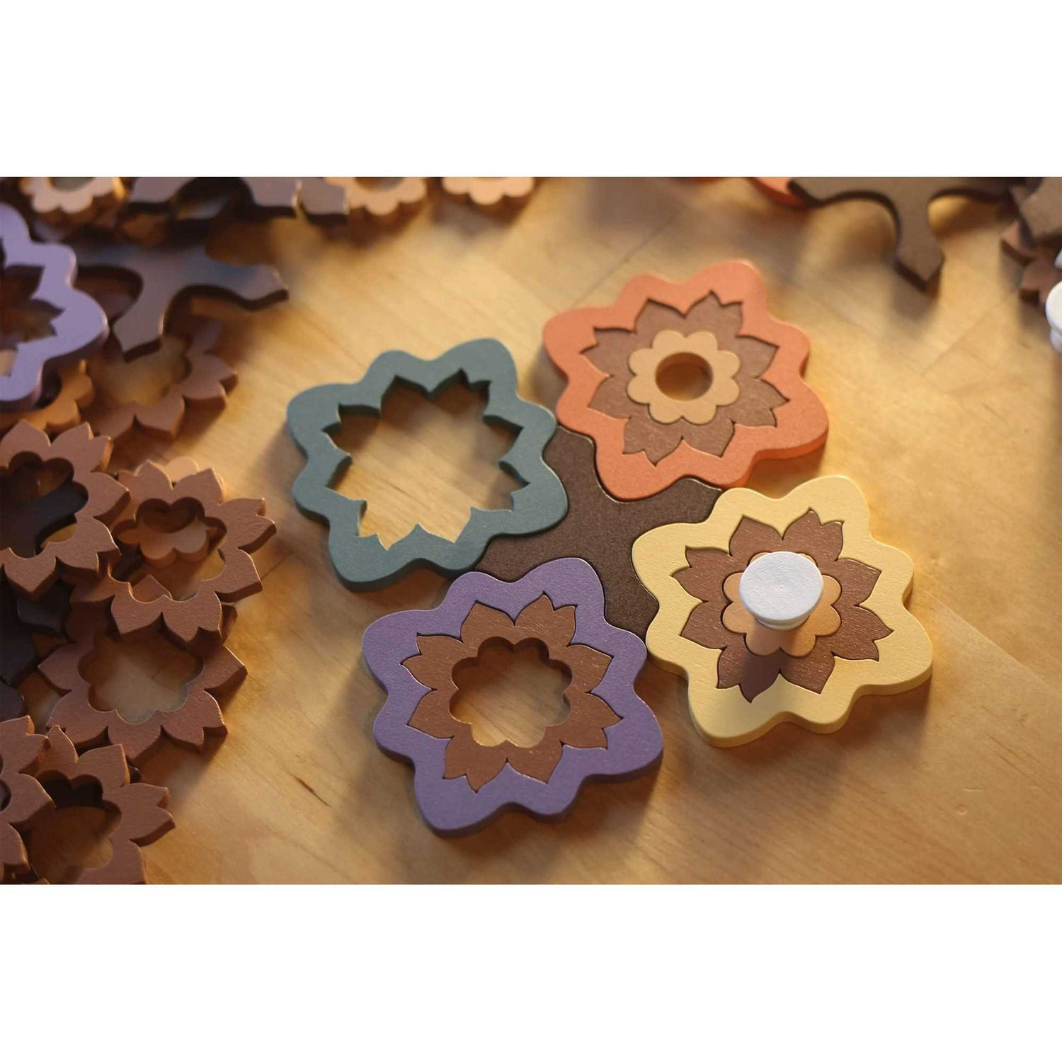 Holzblumen-Puzzleteile in Braun-, Orange-, Grün- und Lilatönen auf einer Holzoberfläche. Einige Teile sind verstreut.