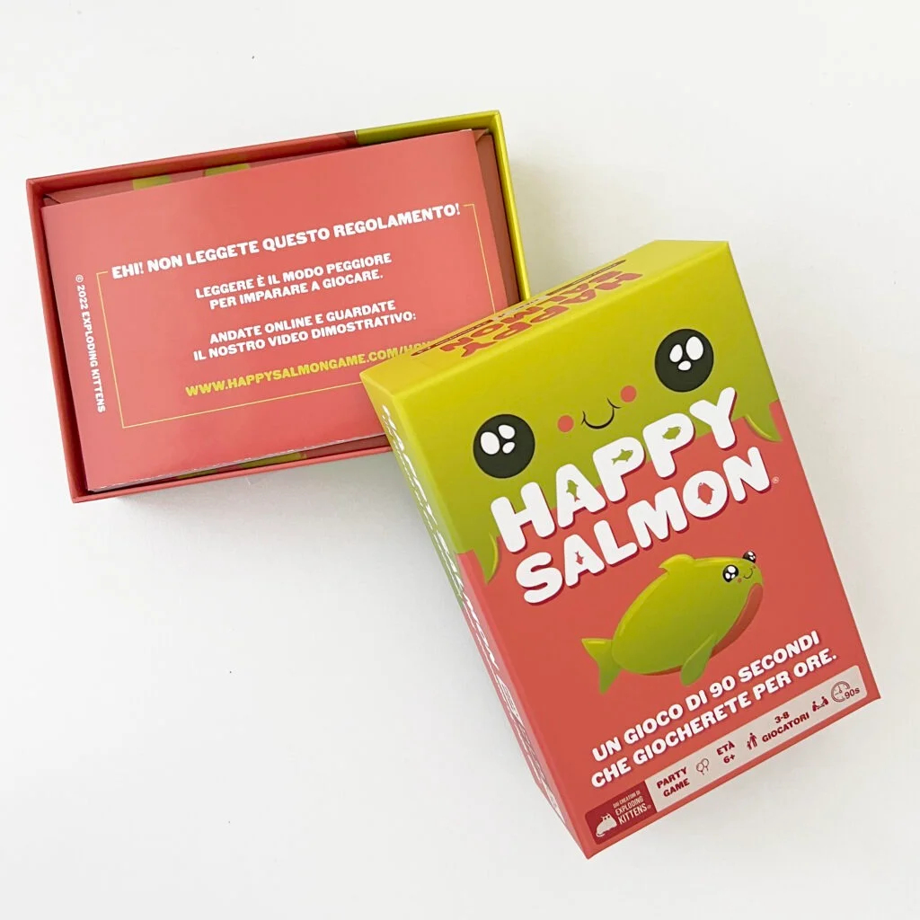 Eine Happy Salmon-Spielbox und die offene Box mit den Anweisungen liegen auf einer weißen Oberfläche.