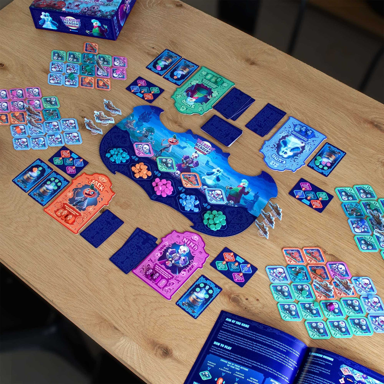 Brettspiel-Setup: Karten, Spielsteine und ein Spielbrett auf einem Holztisch. Box in der oberen linken Ecke.
